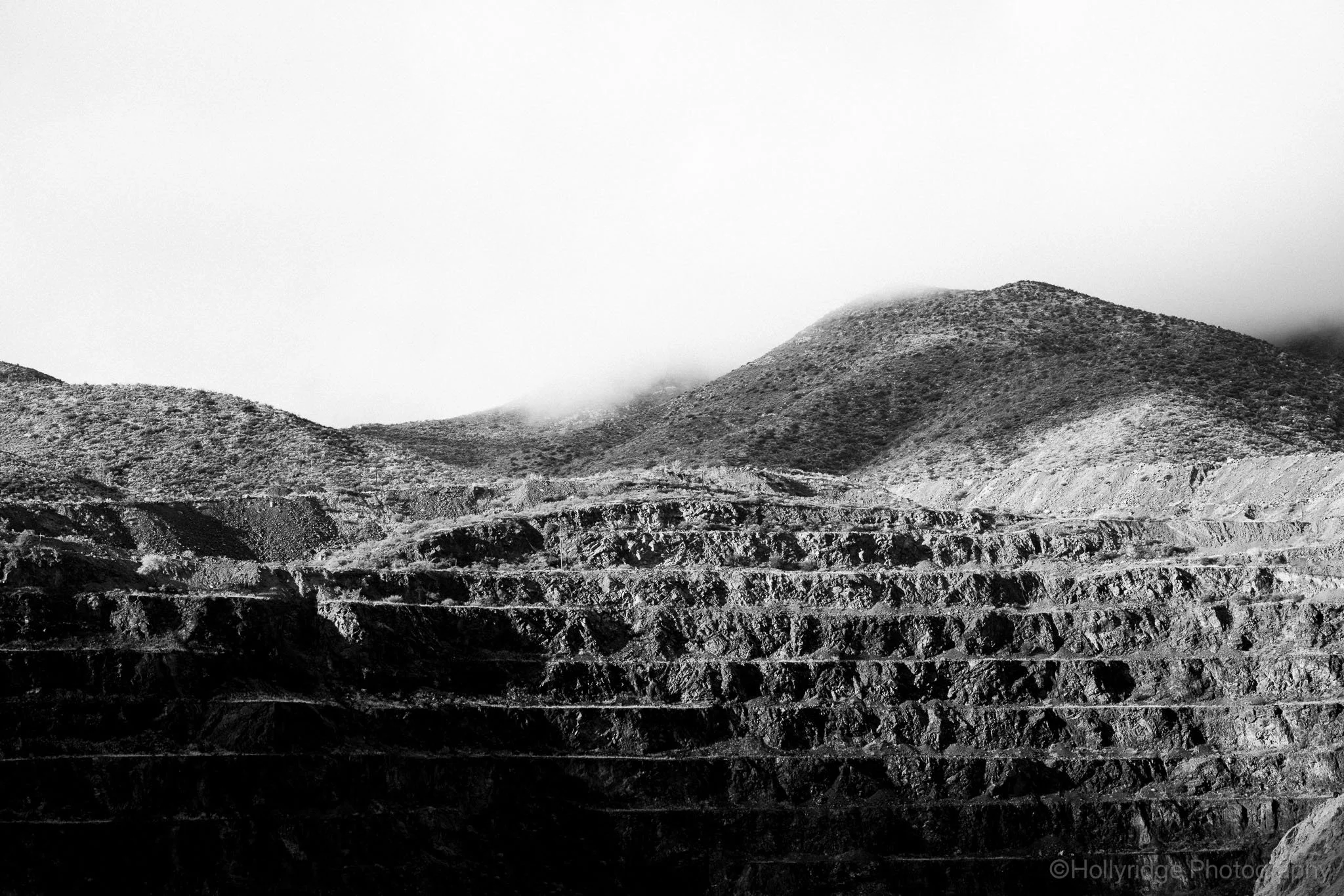 Black and white image of misty mountains above an open pit mine.