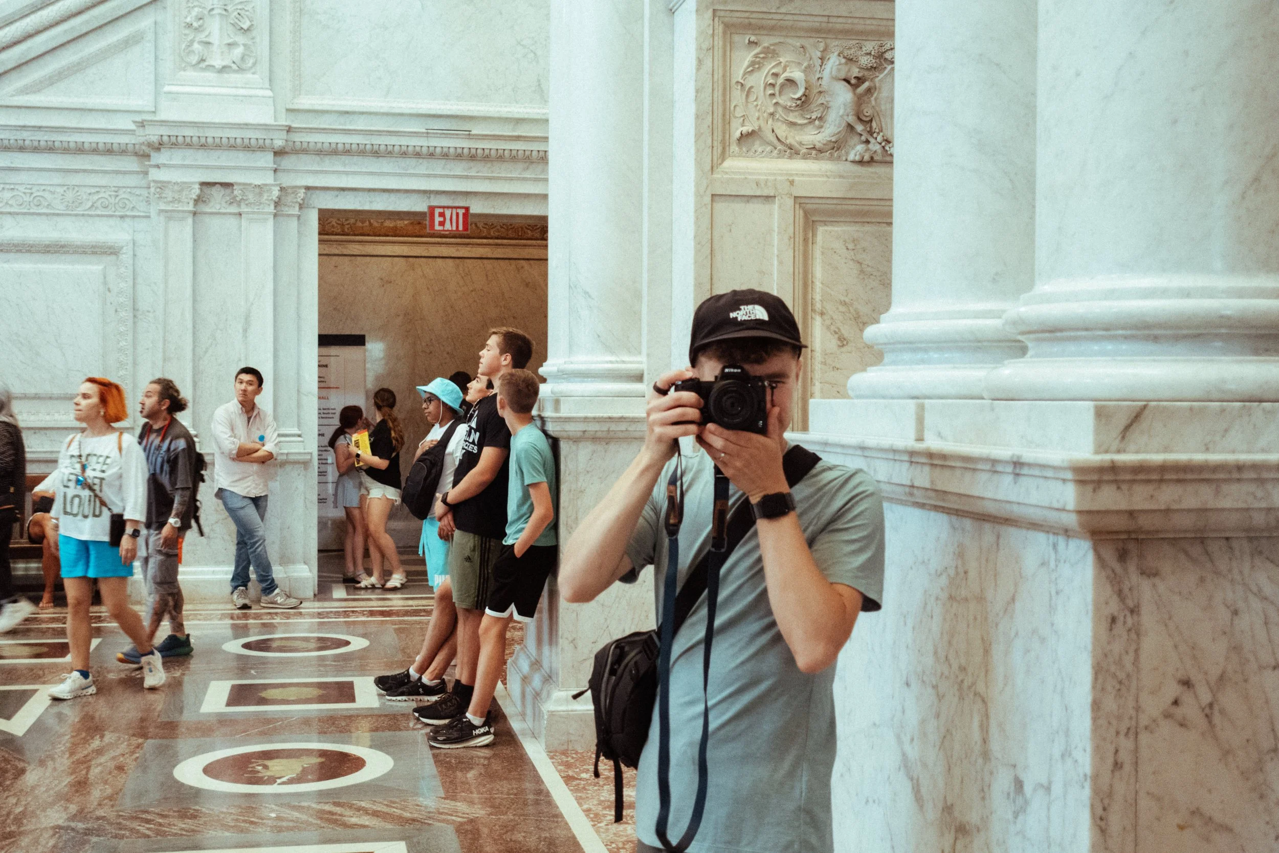 A person taking a photo with a camera inside a grand marble building with other visitors in the background.