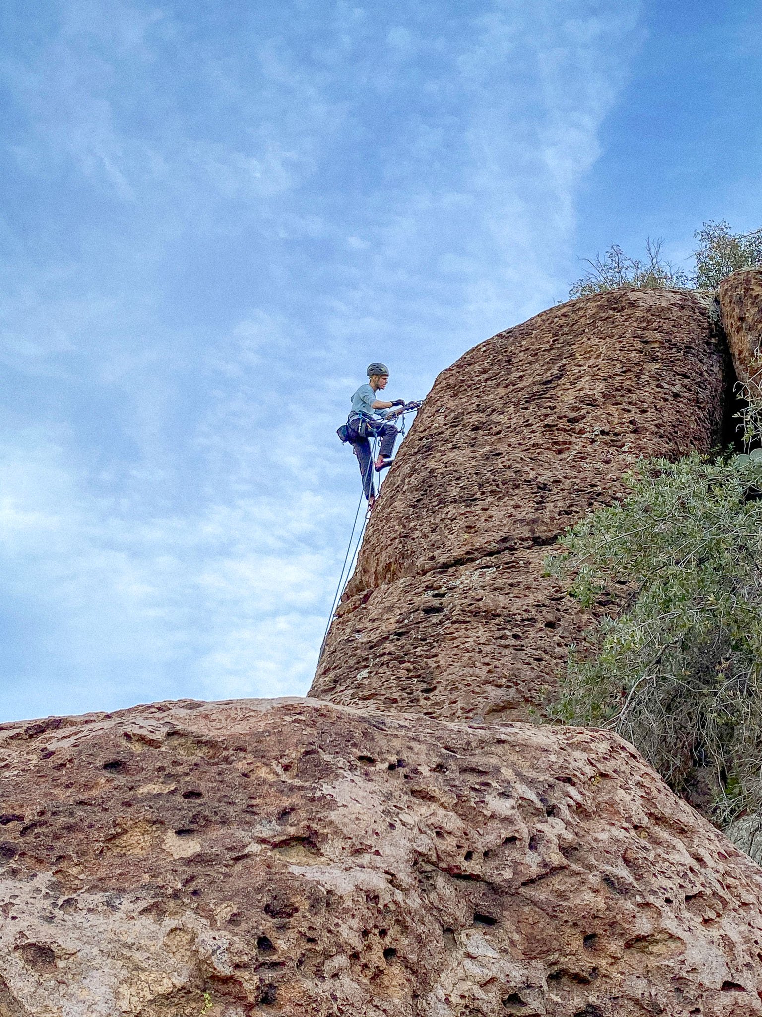 Rock climber ascending volcanic rock formation at The Magma Gardens near Superior Arizona under a bright desert sky