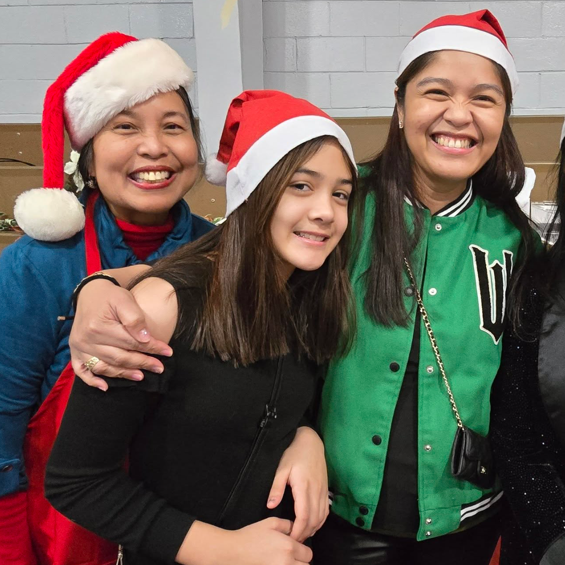 Four women wearing Santa hats smiling and posing together indoors.