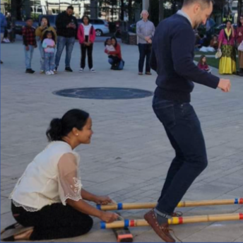 People playing a traditional game with sticks in a park, with onlookers in the background.