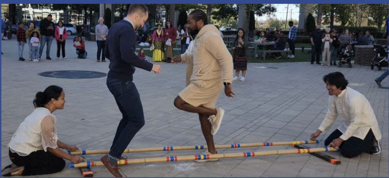 People playing a traditional game with sticks in a park, with onlookers in the background.