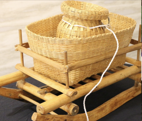 Two woven baskets stacked inside a wooden sled, with a white cord attached to the top basket.