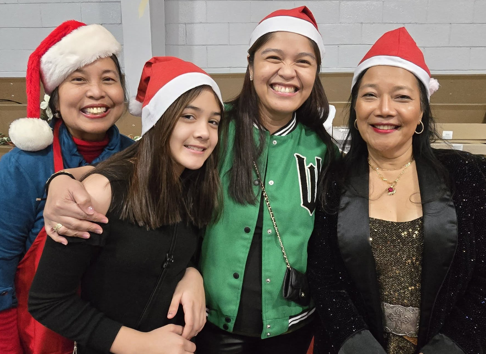Four women wearing Santa hats smiling and posing together indoors.