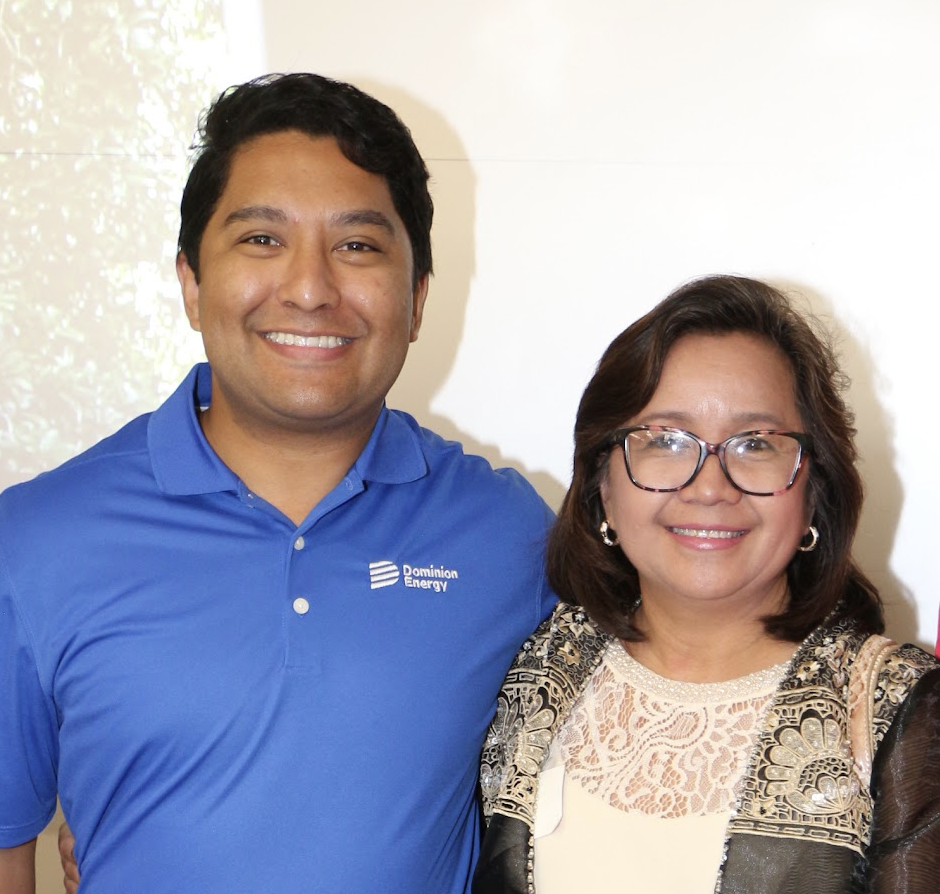 Two people smiling for a photo, a man in a blue polo shirt with 'Dominion Energy' logo and a woman wearing glasses and a patterned top.