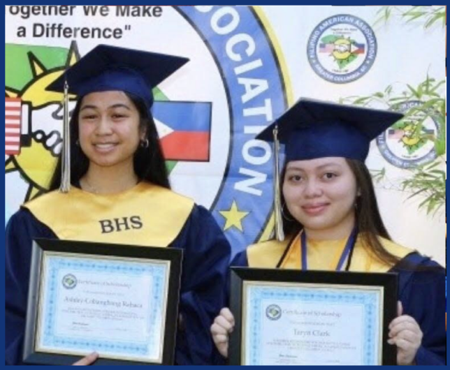 Two female students in graduation caps and gowns holding diplomas at a school ceremony with a banner in the background.