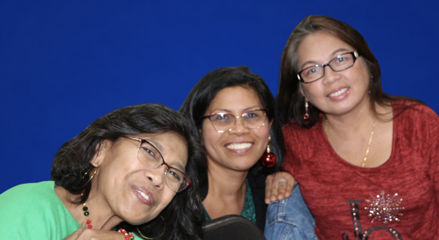 Three women with glasses smiling, posing for a photo against a blue background.