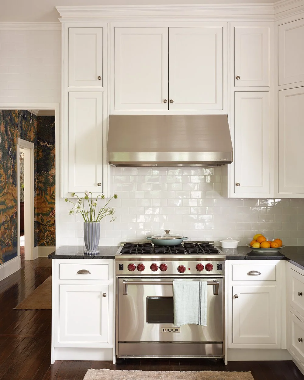 Traditional home kitchen with white cabinetry, black marbled countertops, and silver stove. 