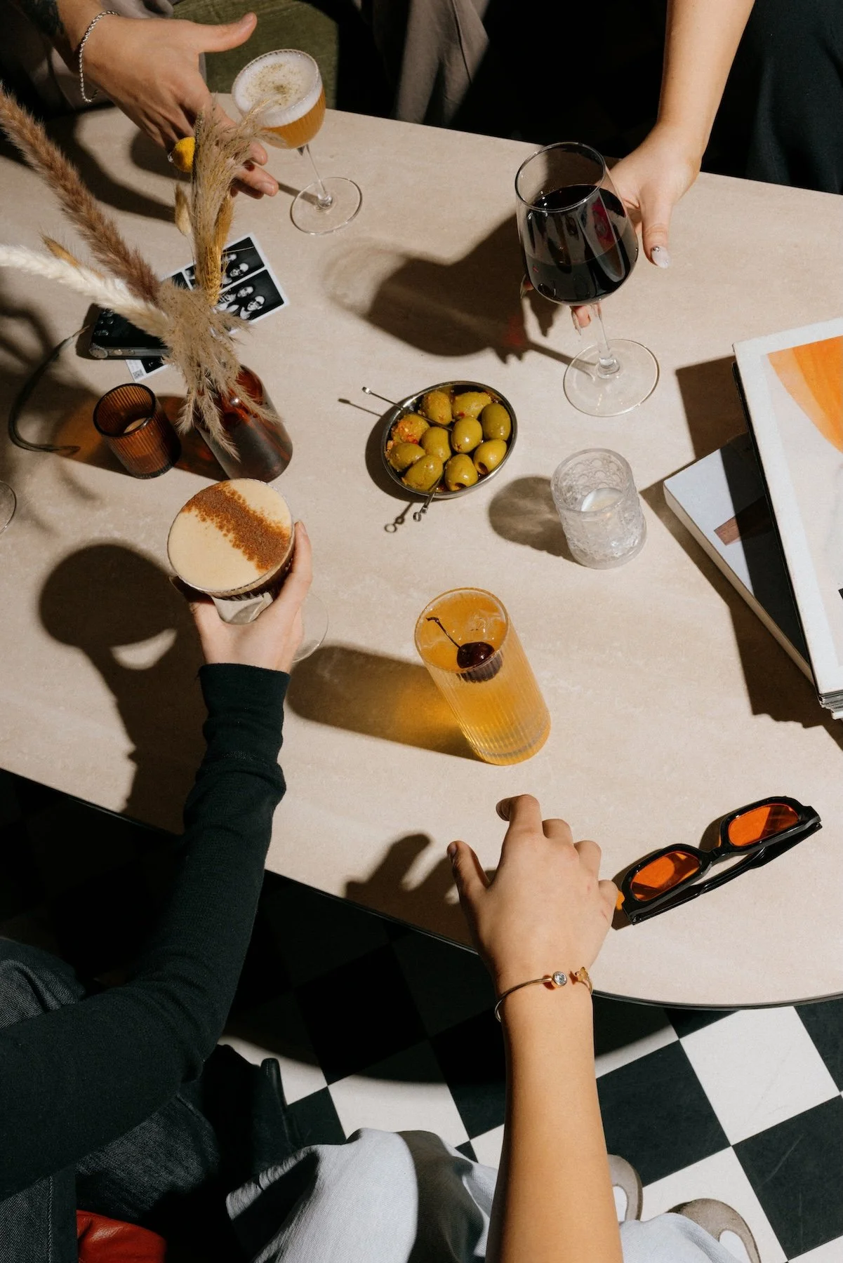 People enjoying drinks and snacks on a table with a black-and-white checkered floor visible underneath.