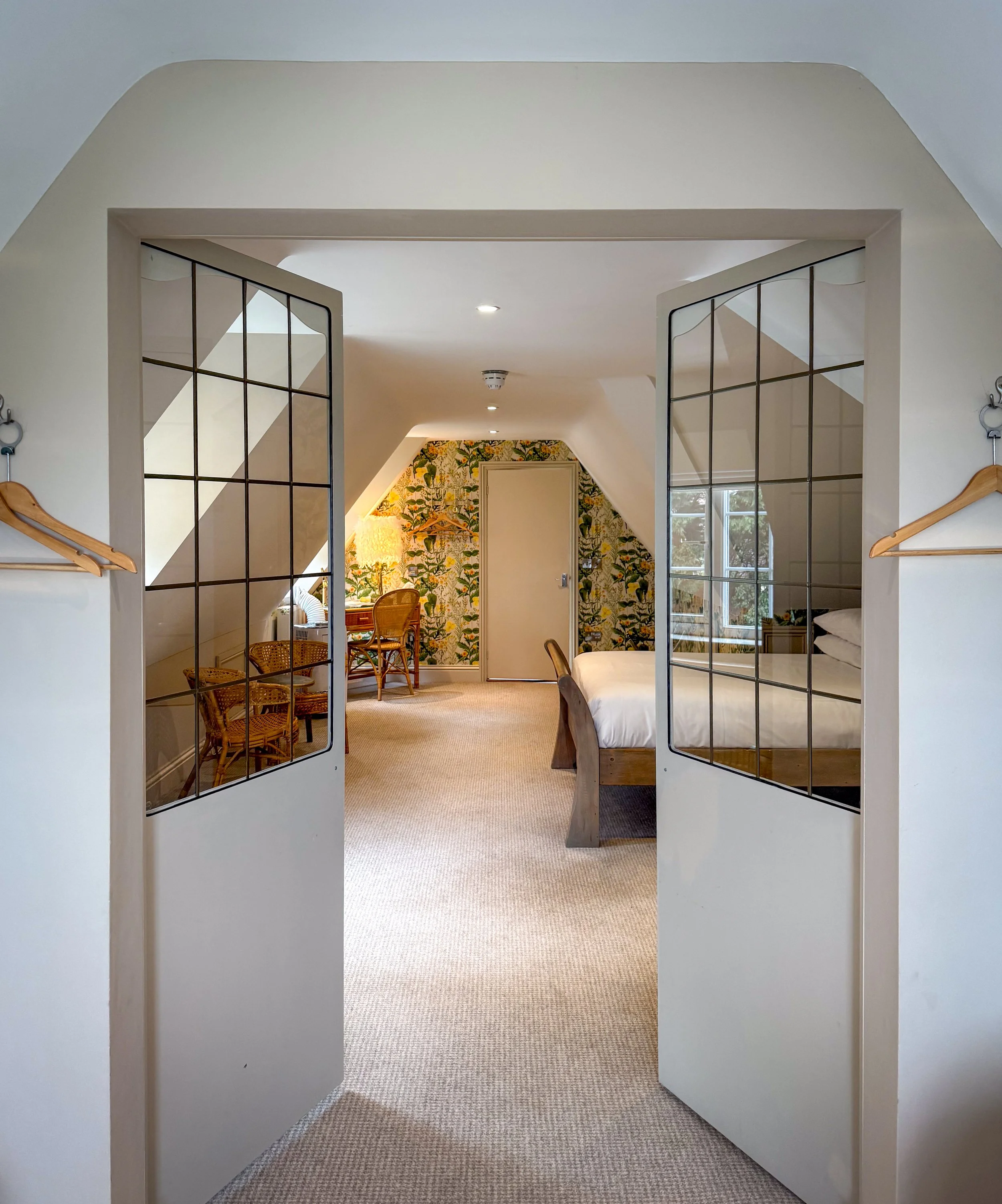 Bedroom with bed, sitting area, floral wallpaper, and windows viewed through open French doors