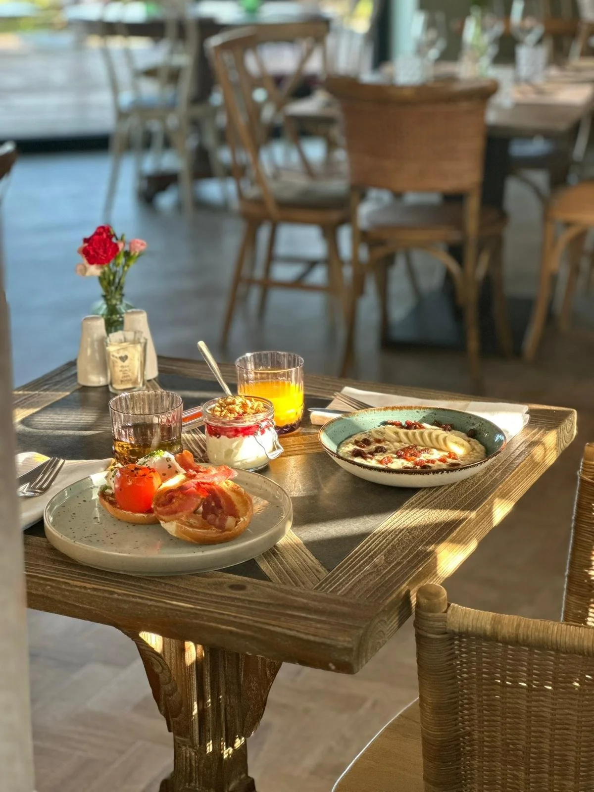 Breakfast table with coffee, yogurt with berries, pastries, and a bowl of pizza, set in a cozy restaurant with wooden tables and chairs.