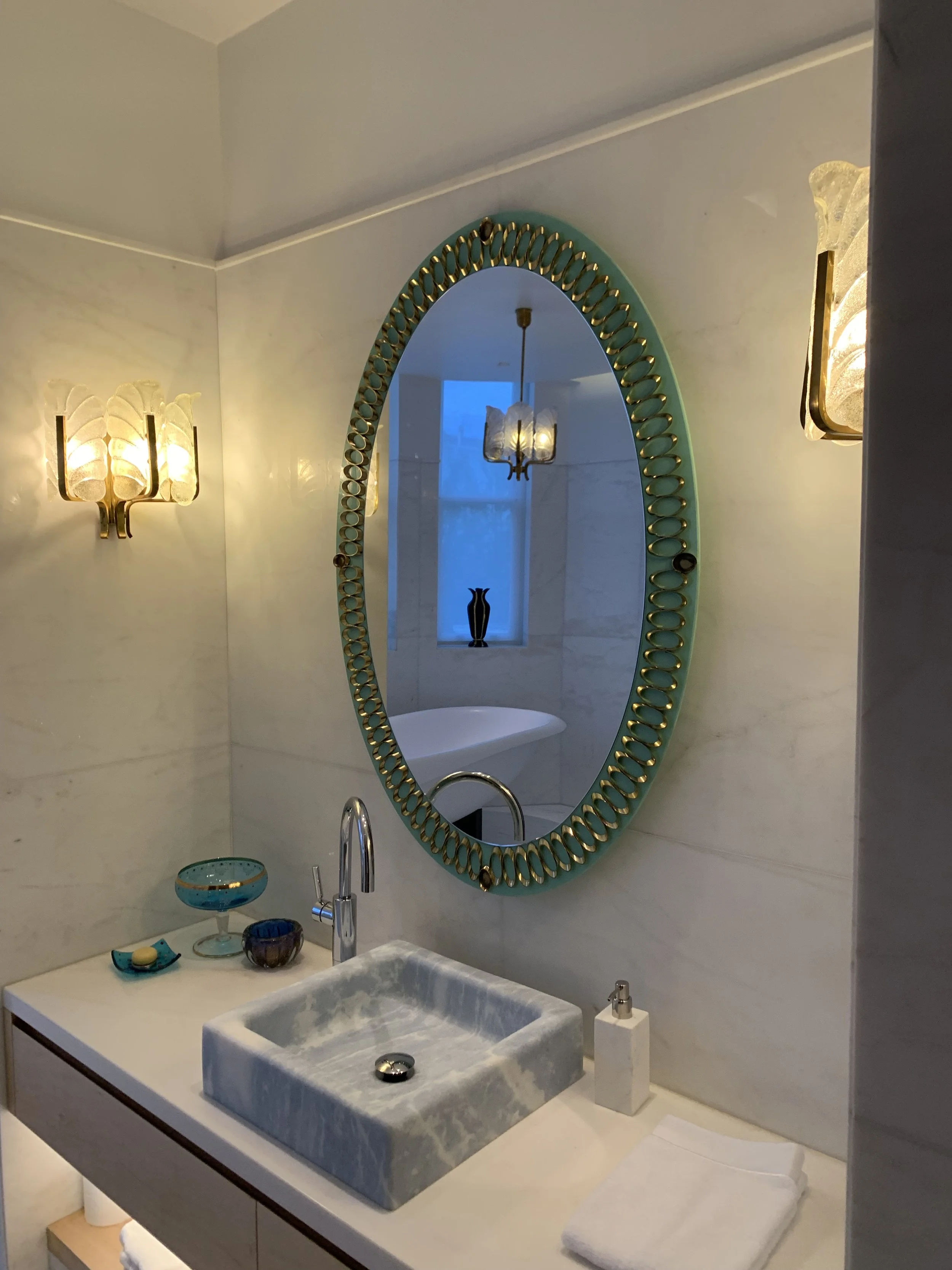 Bathroom sink with a marble basin, above a mirror with a decorative frame, and wall-mounted light fixtures on each side.


