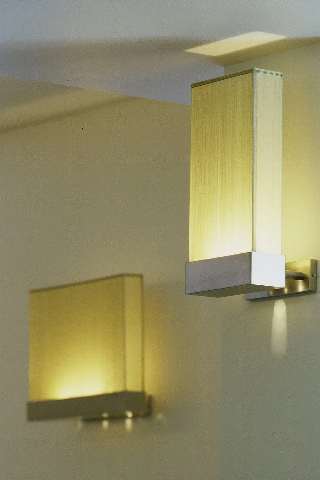 Two modern wall-mounted light fixtures with yellowish diffusers on a light-colored wall.


