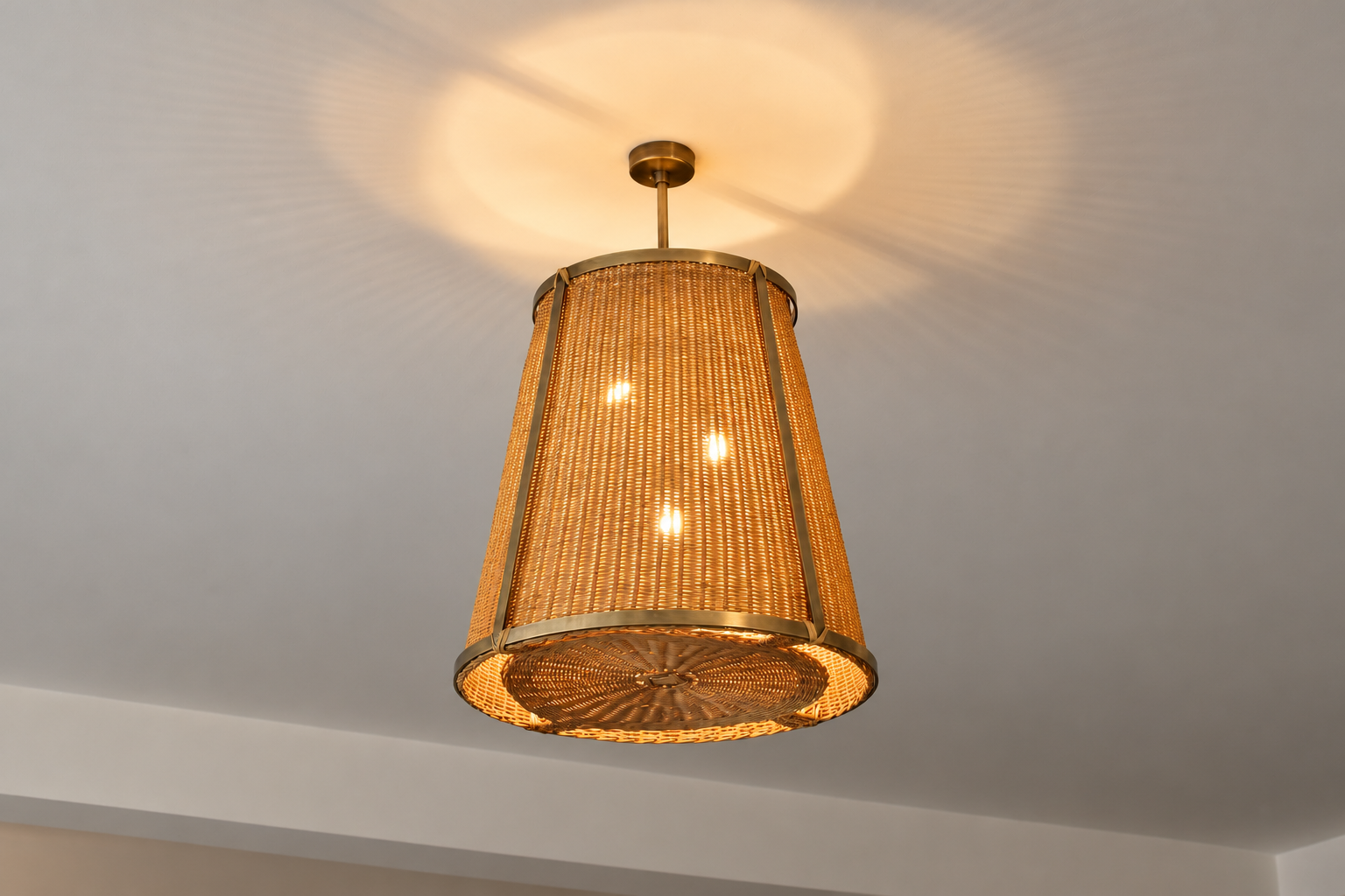 The Caeli-SD contemporary handcrafted made-to-measure pendant light fixture features an expertly handcrafted brass structure and a hand-woven dark-tinted rattan shade. 