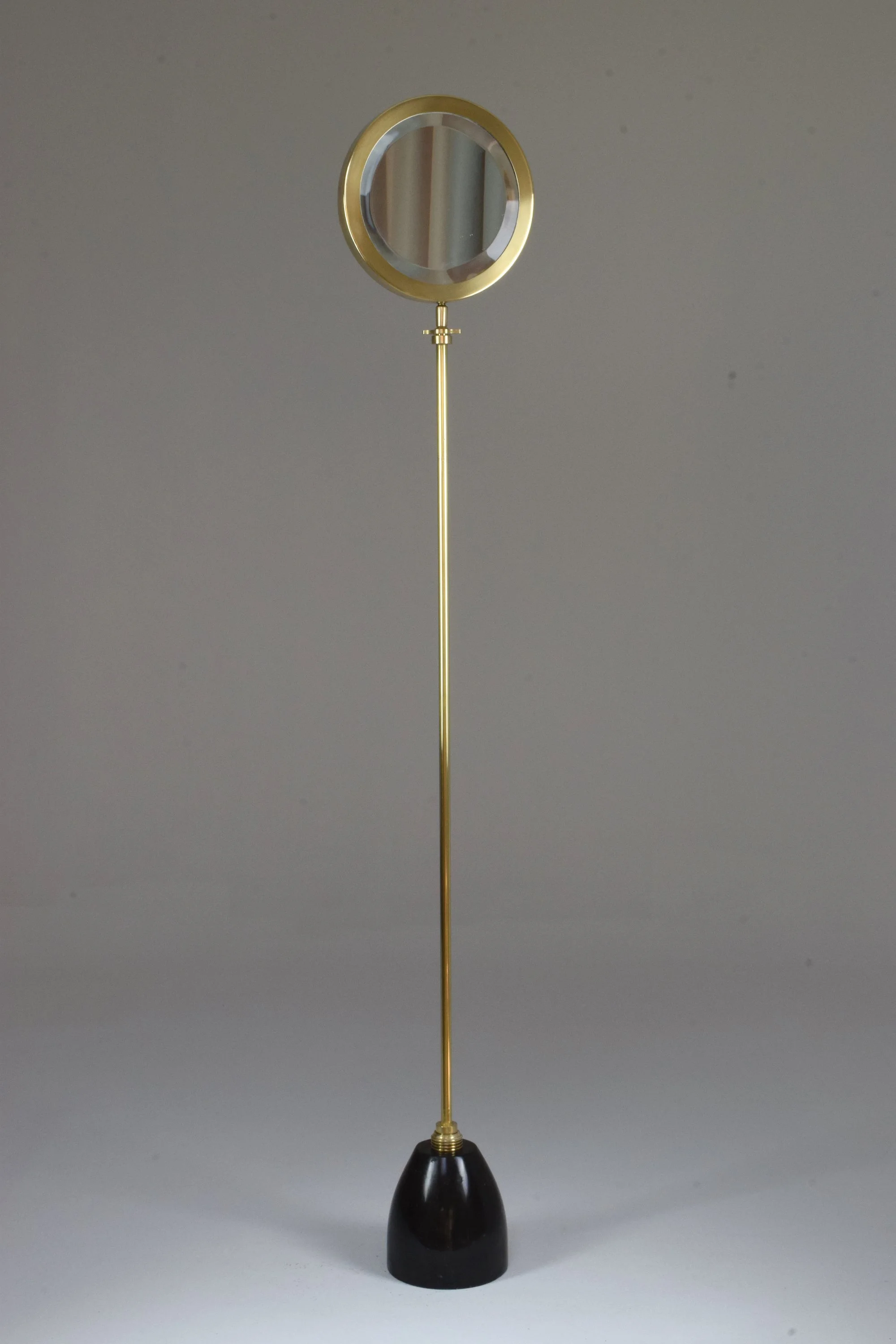 Handcrafted standing mirror designed with a solid gold brass structure, a circular mirror frame, and a black marble base.
 
The Conscious Confinement Collection is a unique series of lights, tables, and decorative objects designed by Jonathan Amar St