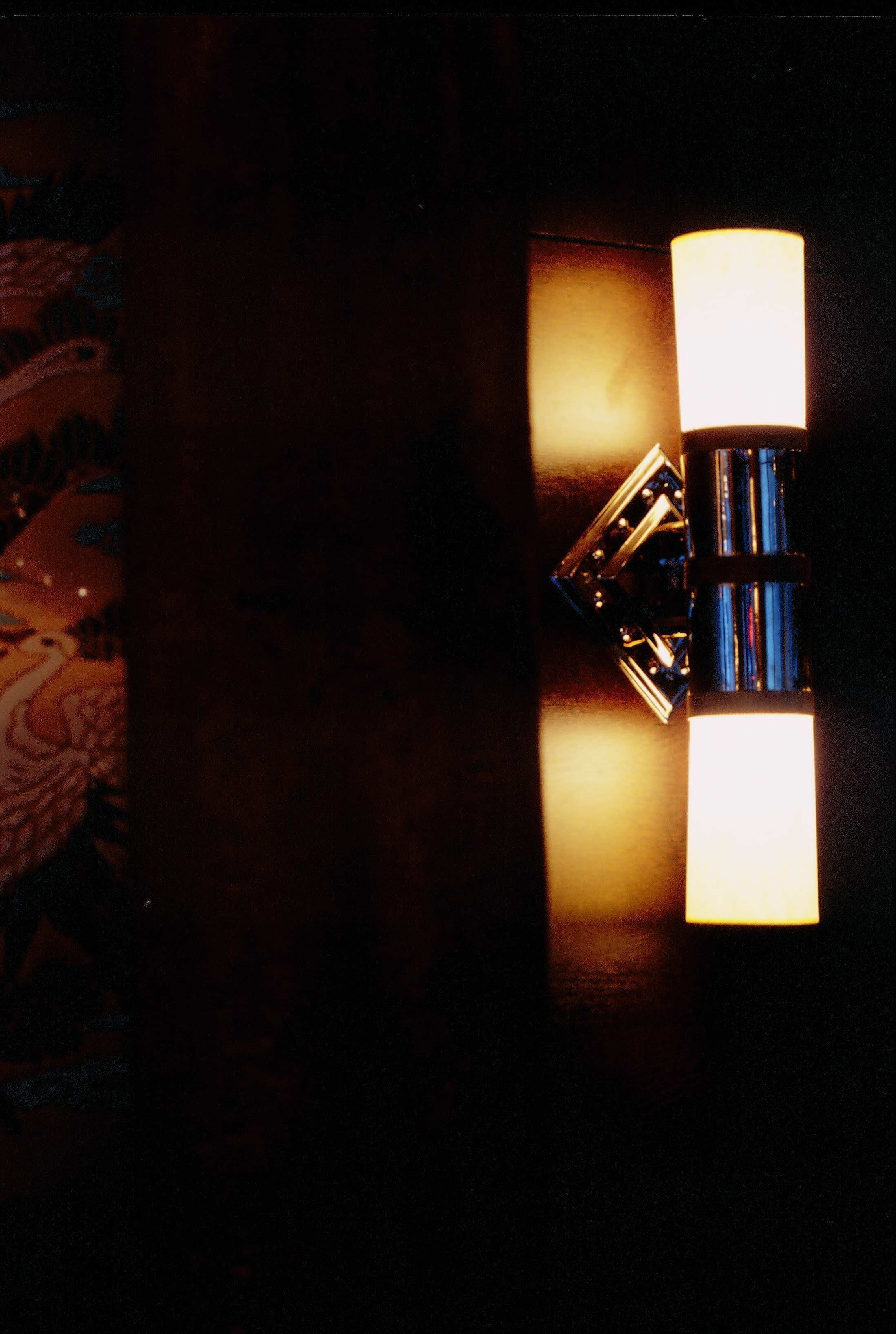 Wall-mounted light fixture with two illuminated rectangular lamps on a dark wall.


