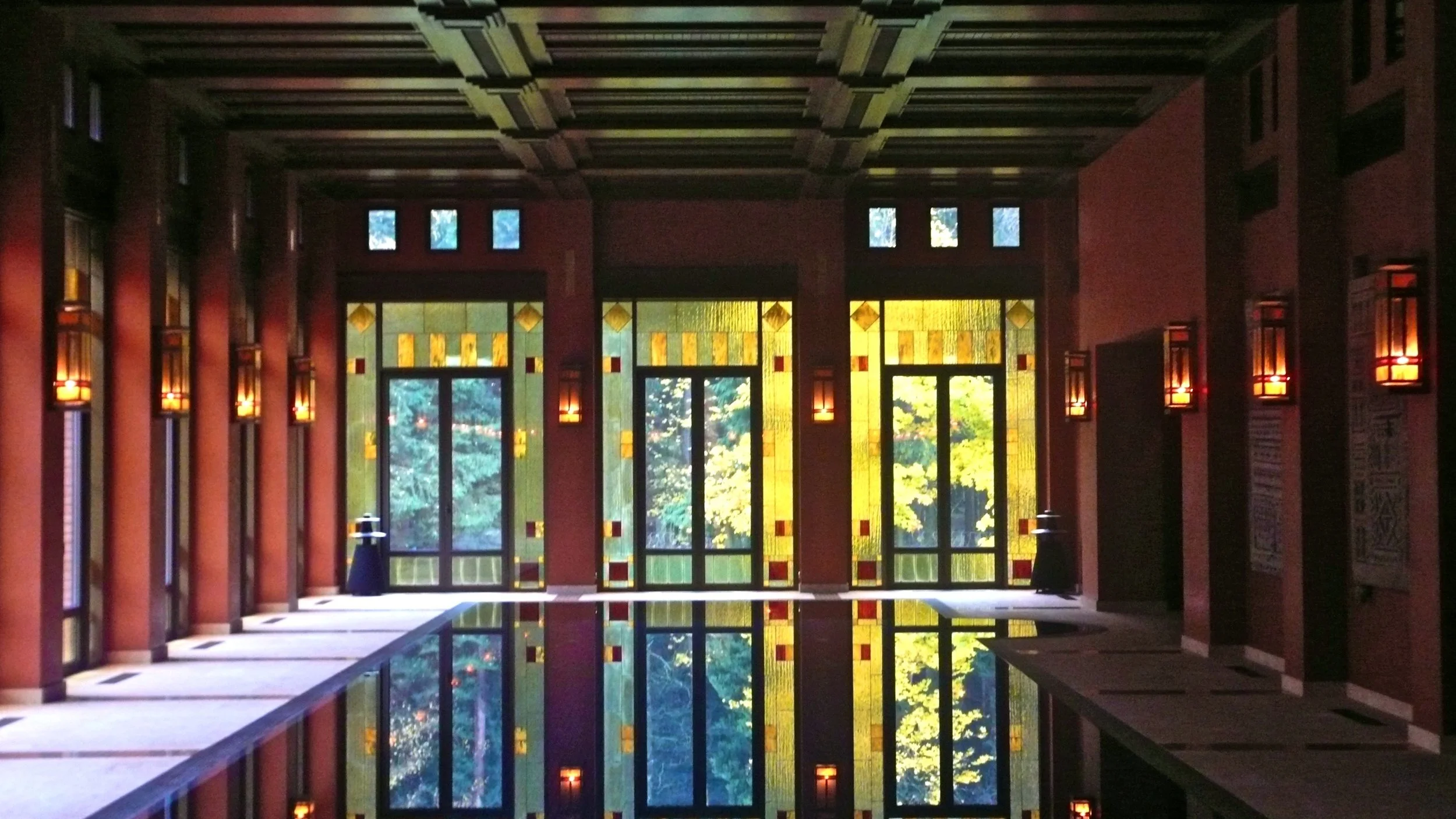 Interior of a room with large stained glass windows, red brick walls, and a reflective pool on the floor.


