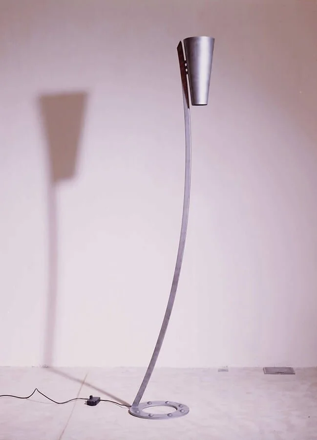 A modern, curved-standing floor lamp with a metallic finish, casting a shadow on the wall behind it.