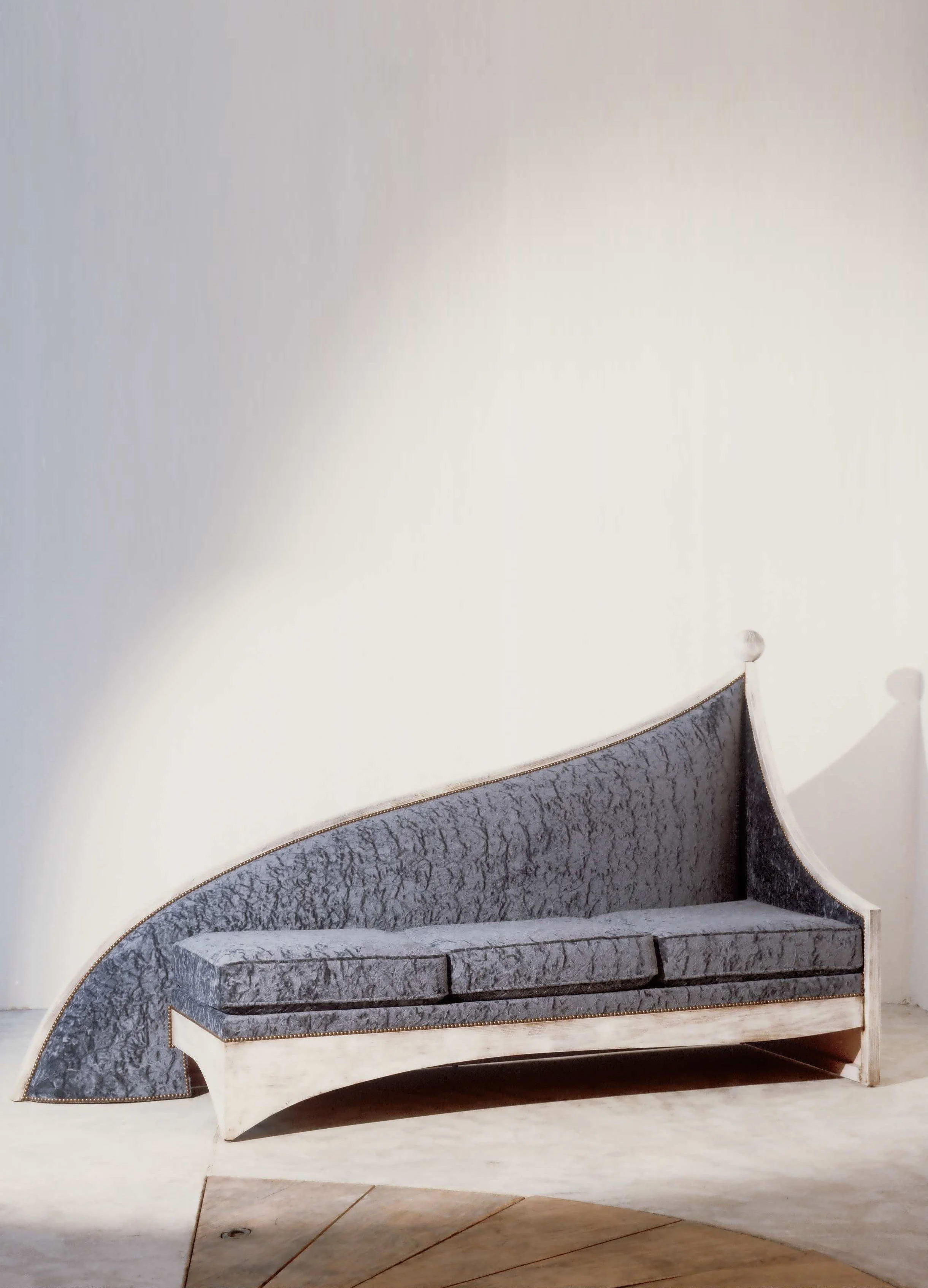 A modern, curved sofa with grey patterned upholstery and a light wooden frame, placed against a plain white wall.



