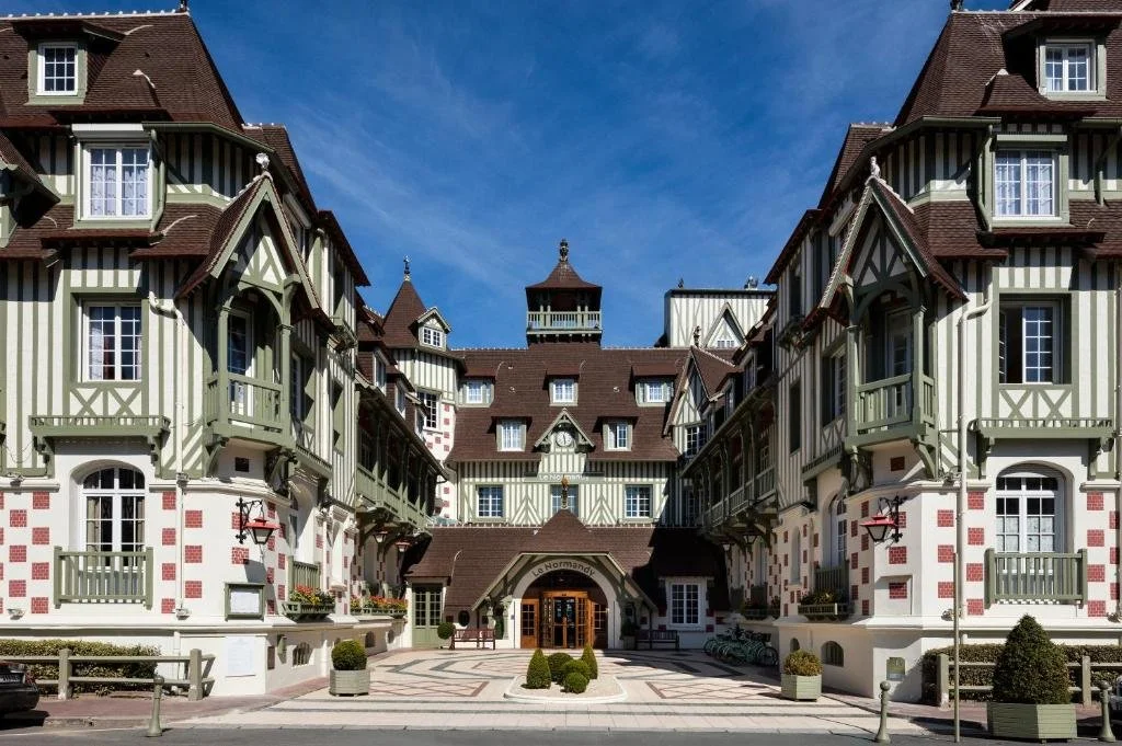 A large, ornate building designed in a European architectural style with multiple stories, steep roofs, and decorative woodwork. The building features French windows, small balconies, and a central archway entrance.