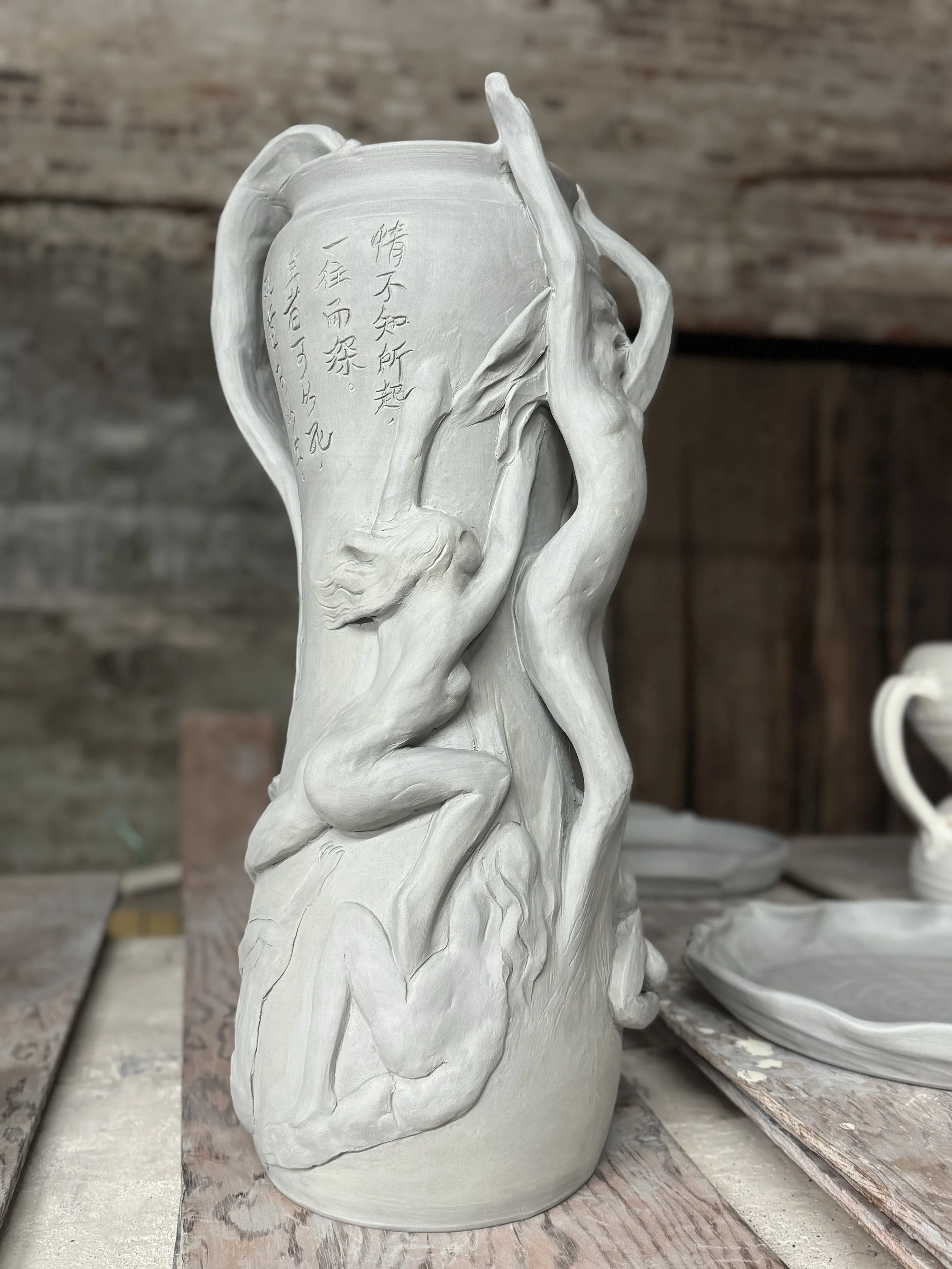 A ceramic sculpture of a human face with intricate facial features, surrounded by flowing, organic shapes, with Asian characters inscribed on one side.