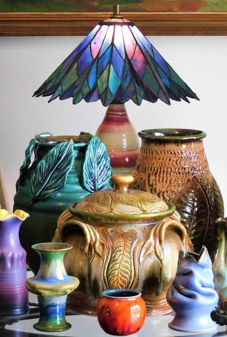 A collection of colorful decorative ceramic vases and a stained glass lamp with a purple, blue, and pink petal design.