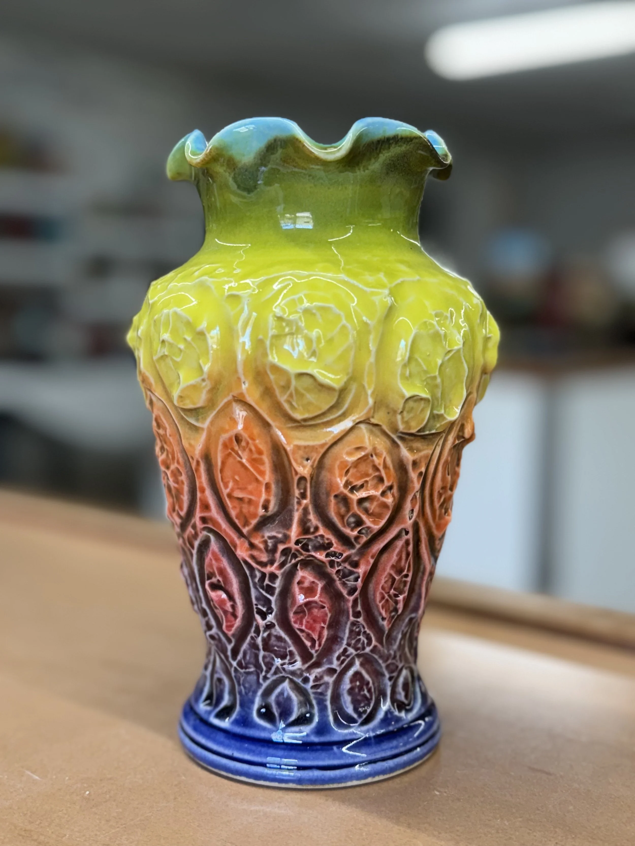 Colorful ceramic vase with a textured, intricate pattern, transitioning from green at the top to red and blue at the bottom.