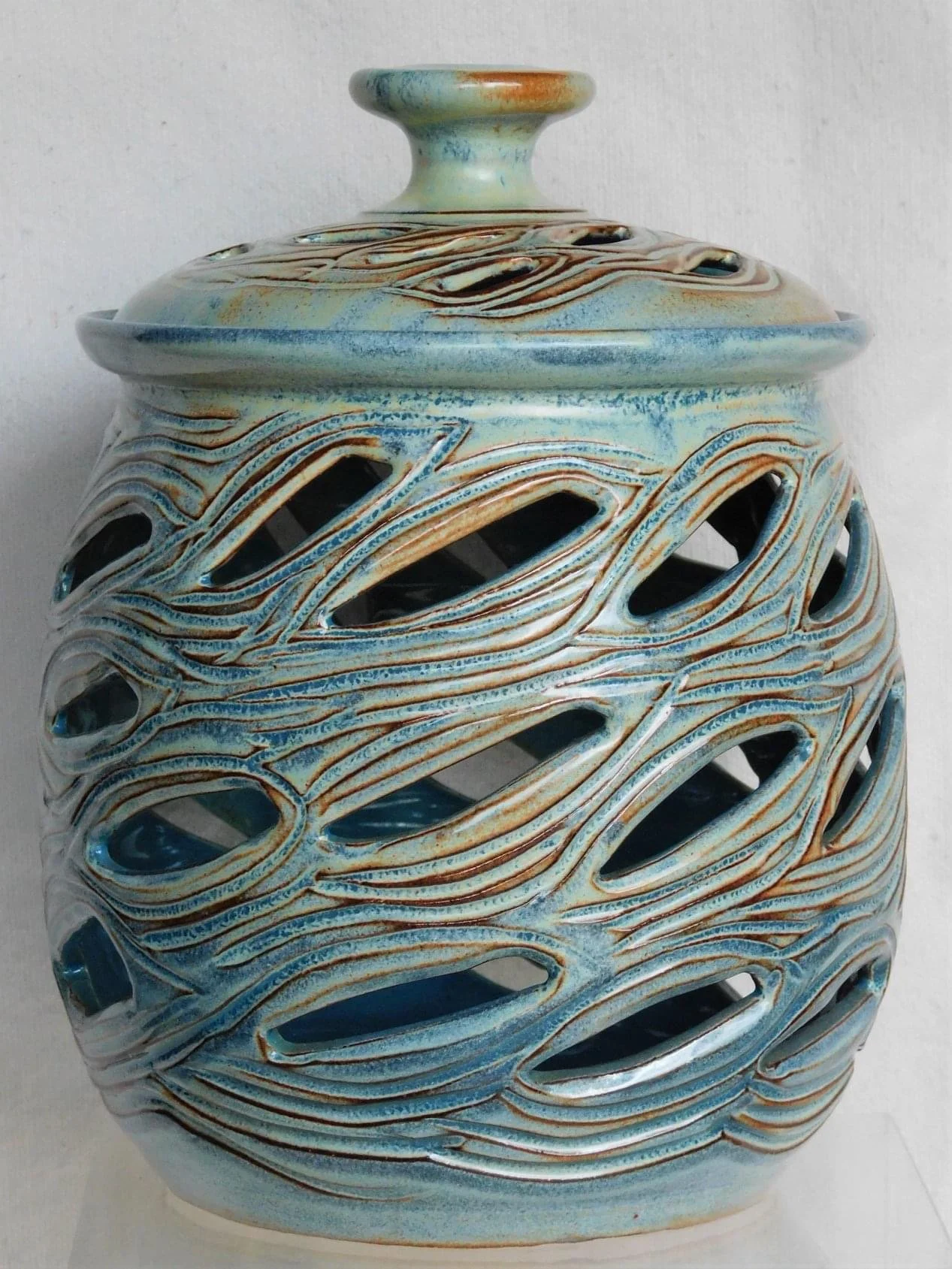 Decorative ceramic vase with cut-out swirling patterns, glazed in shades of blue, brown, and cream.