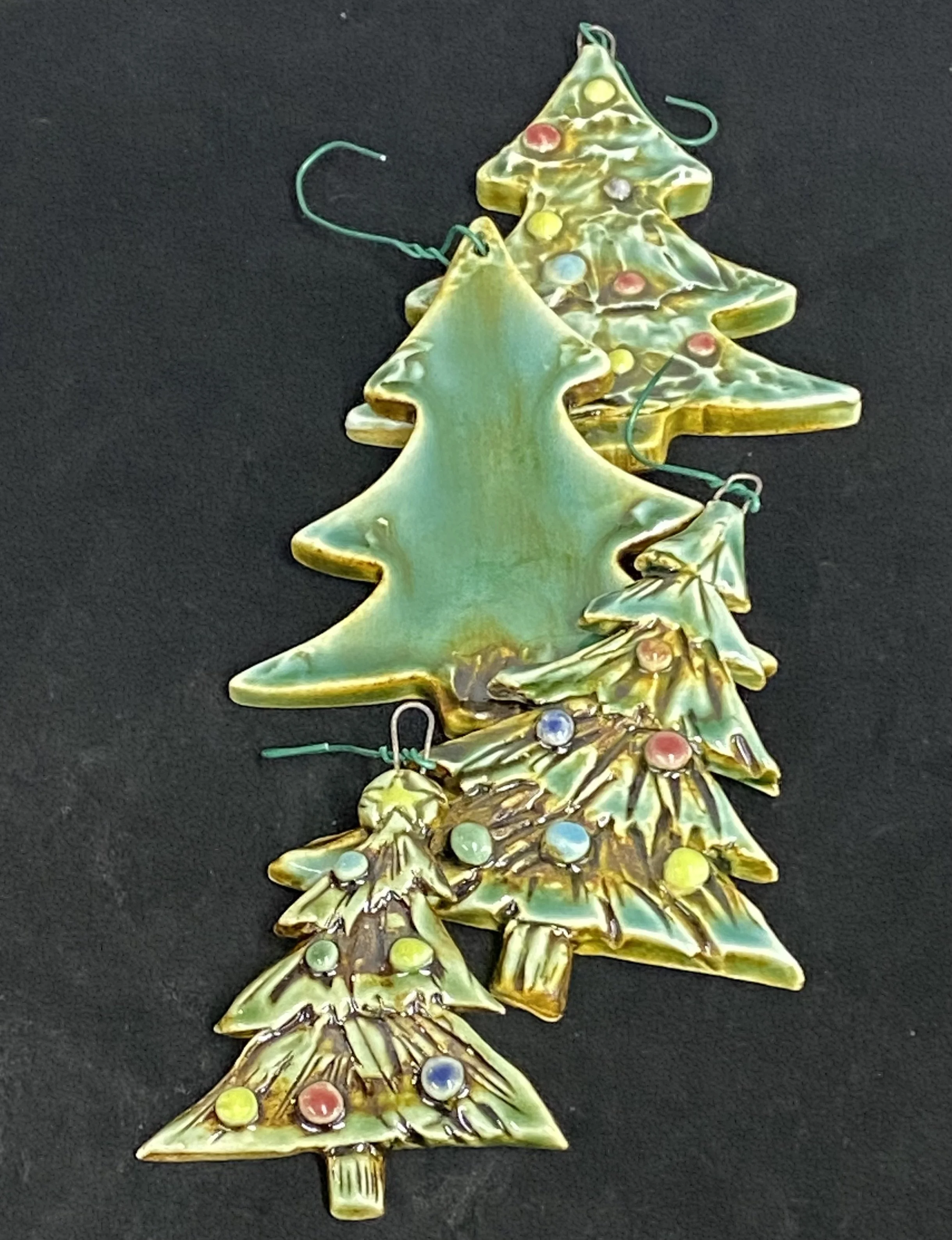 Set of decorative Christmas tree ornaments with a glassy, gold-edged, green finish, decorated with small colorful beads, on a black background.