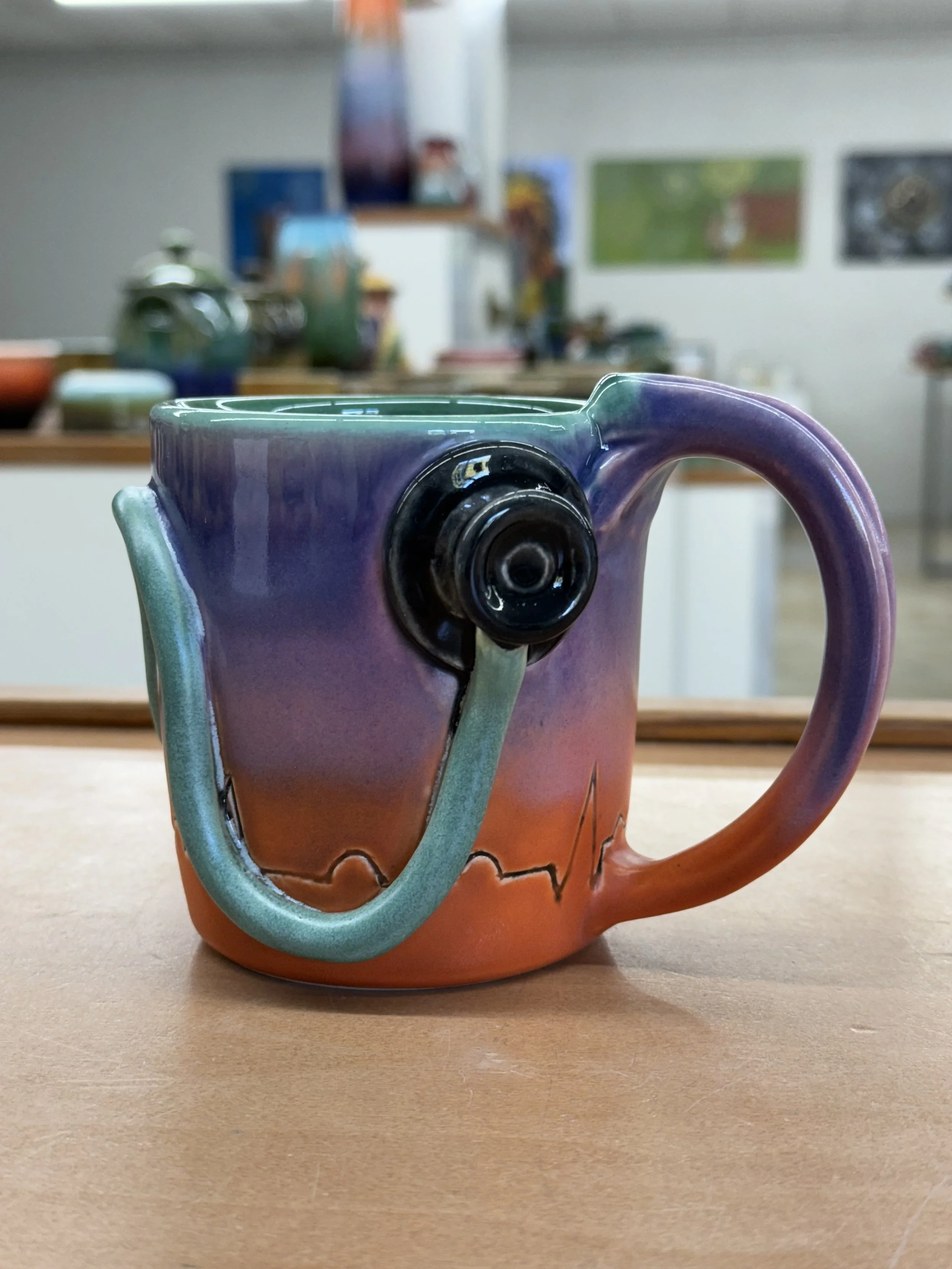 Colorful ceramic mug with a stethoscope design on a table in an art studio.