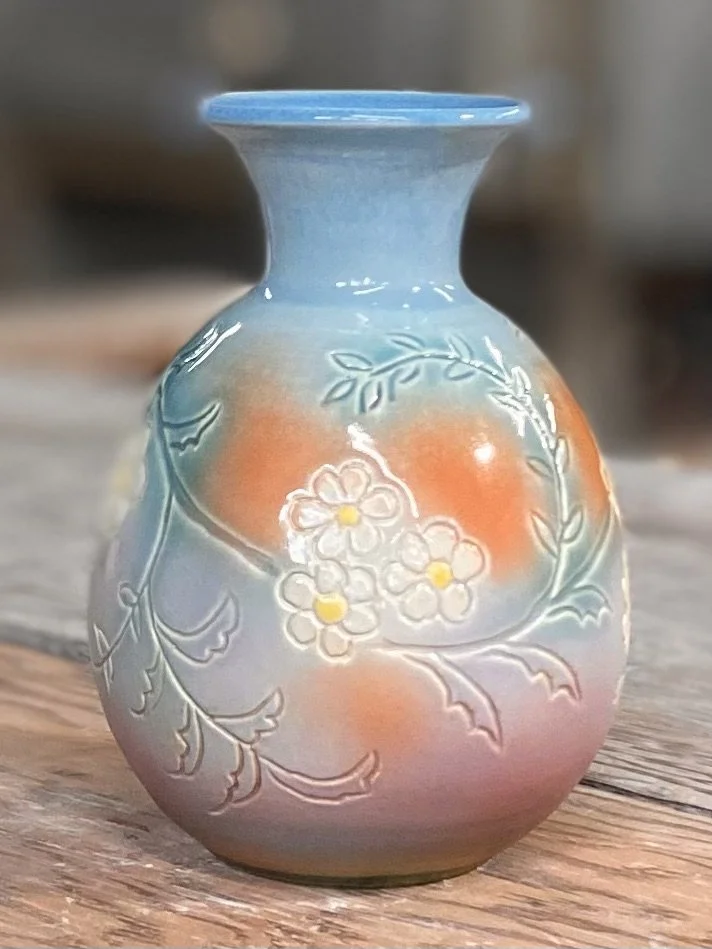 A small decorative ceramic vase with a pastel gradient of blue, pink, and white, featuring embossed floral and leafy patterns.