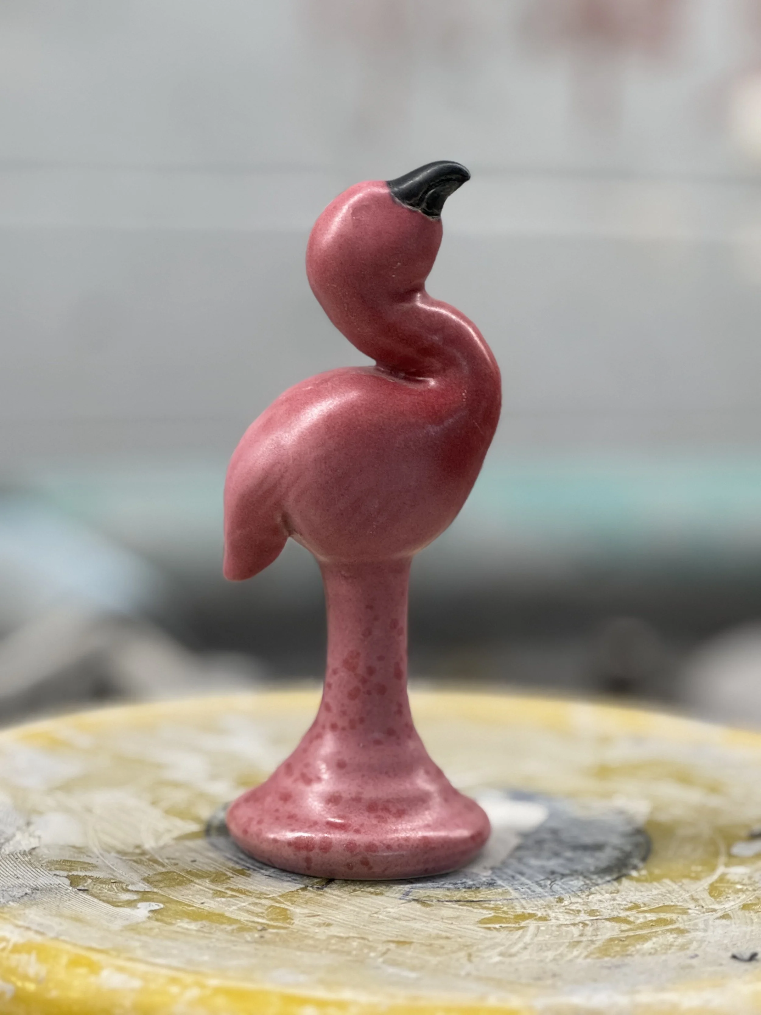 Pink flamingo figurine with black beak on a textured surface.