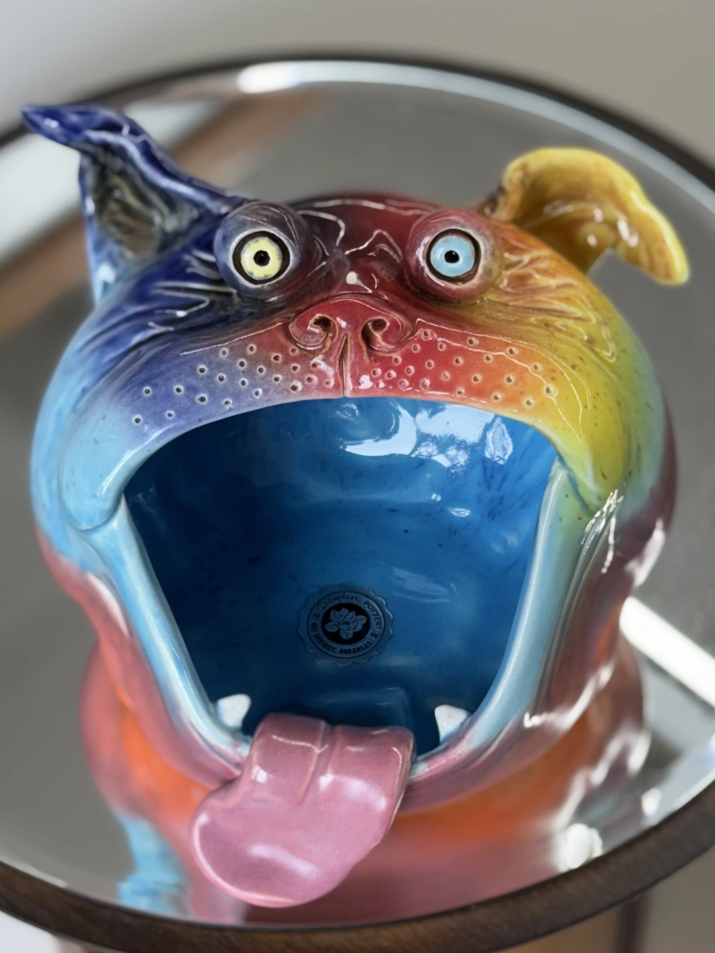 Colorful ceramic dog head designed with wide open mouth, tongue sticking out, and playful eyes, featuring a rainbow of colors including blue, red, yellow, and orange.