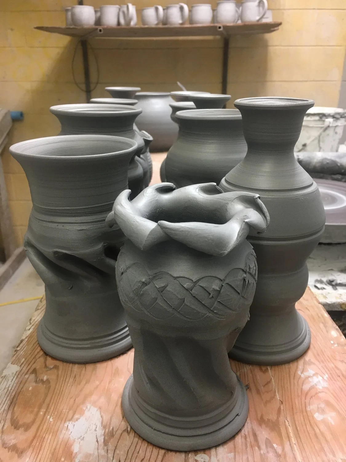 Unfinished pottery vases and bowls on a wooden workbench in a ceramics studio.