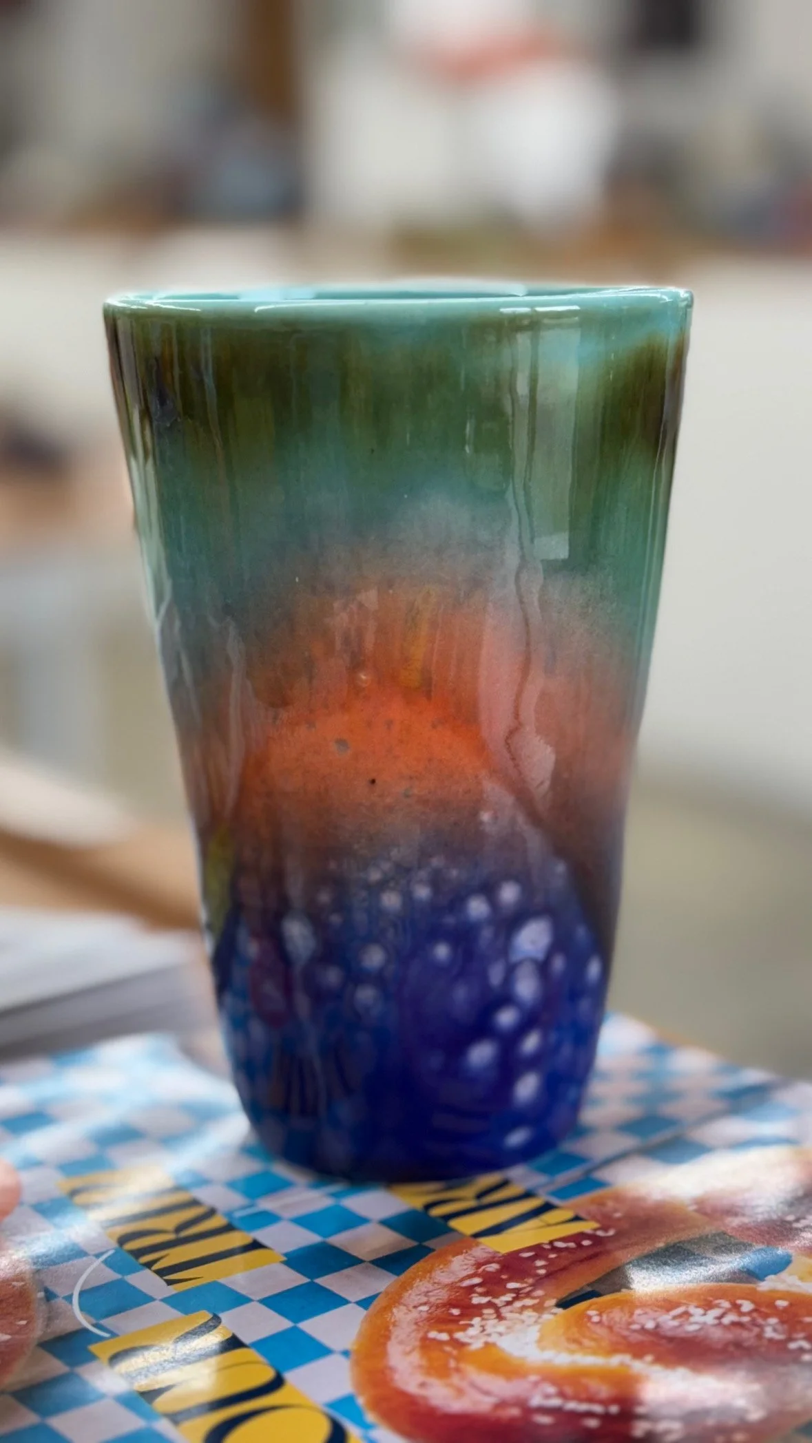 Close-up of a colorful painted ceramic vase on a table with a magazine underneath.
