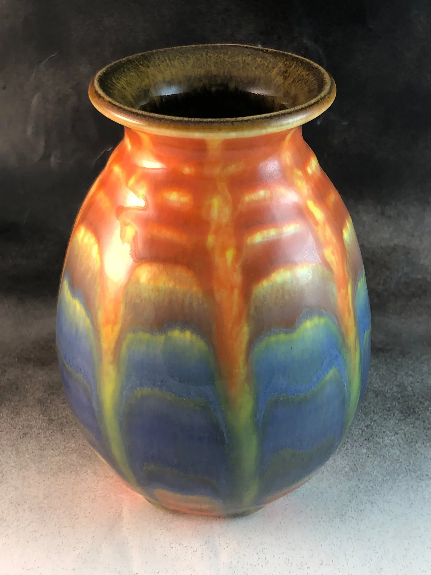 Colorful ceramic vase with a glossy finish and a dark center set against a black background.