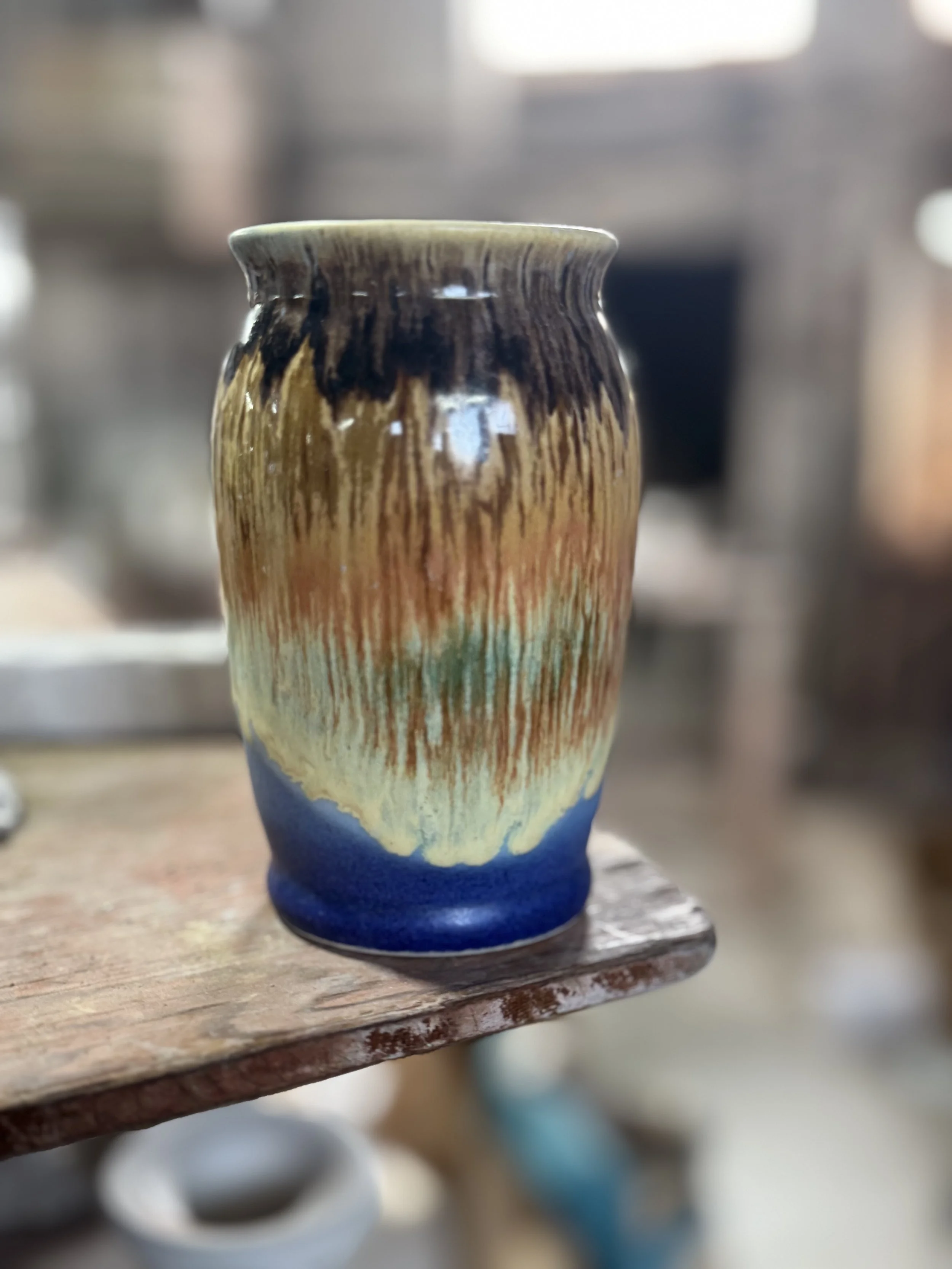 Colorful ceramic vase with a textured glaze, placed on a wooden surface with a blurred background.