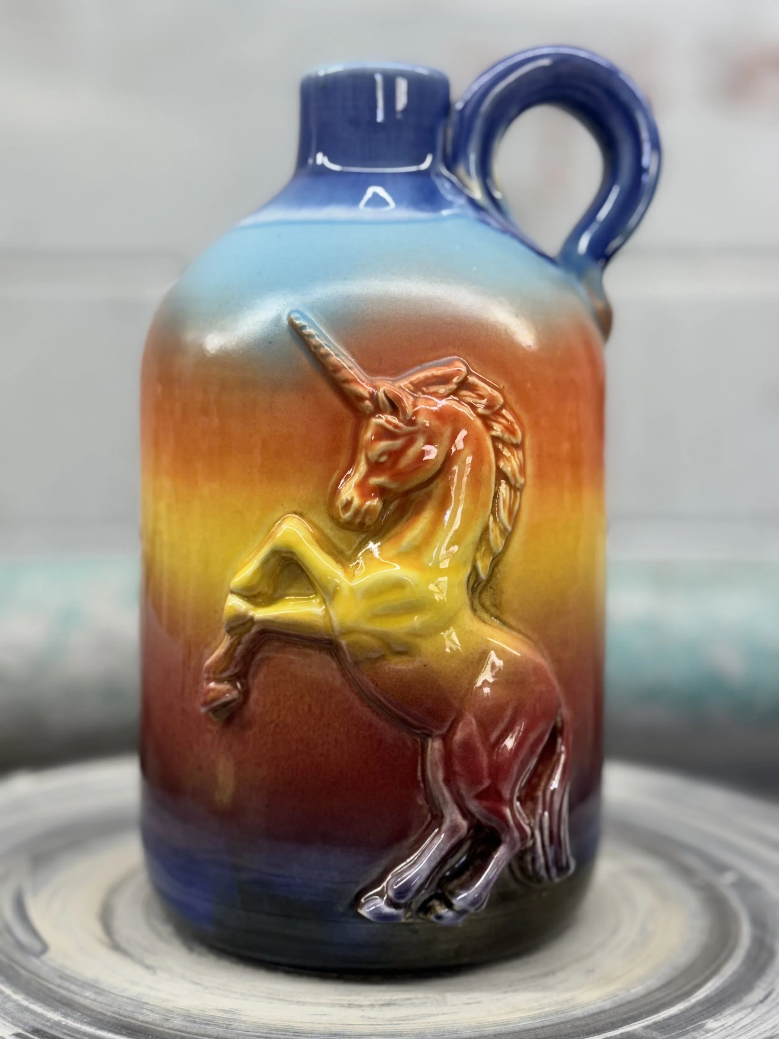Colorful ceramic vase with a 3D raised unicorn design, transitioning from blue at the top, through orange and yellow, to dark blue at the bottom.