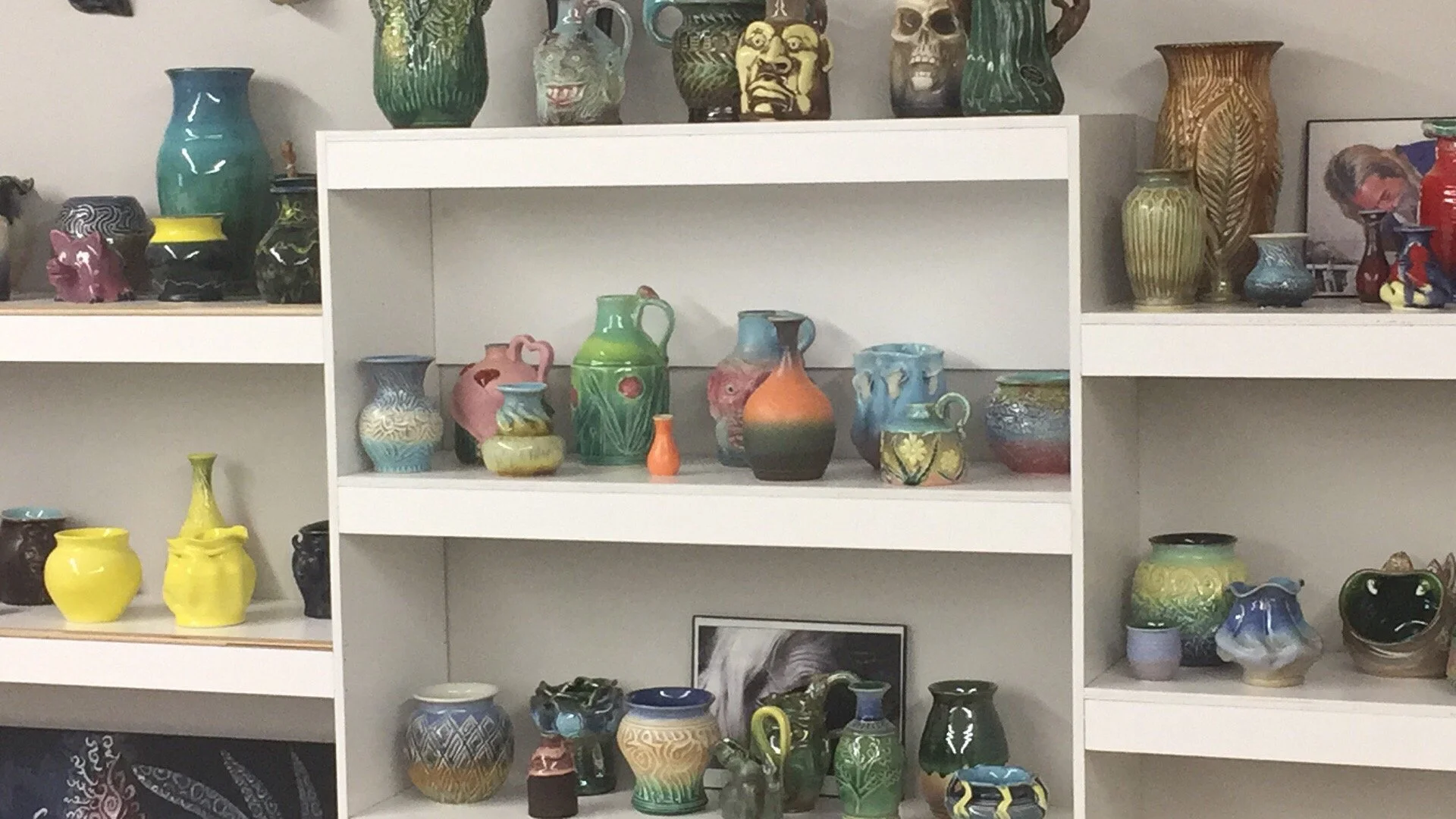 Display of assorted colorful vases and pottery on white shelves, featuring various shapes, sizes, and glazed patterns.