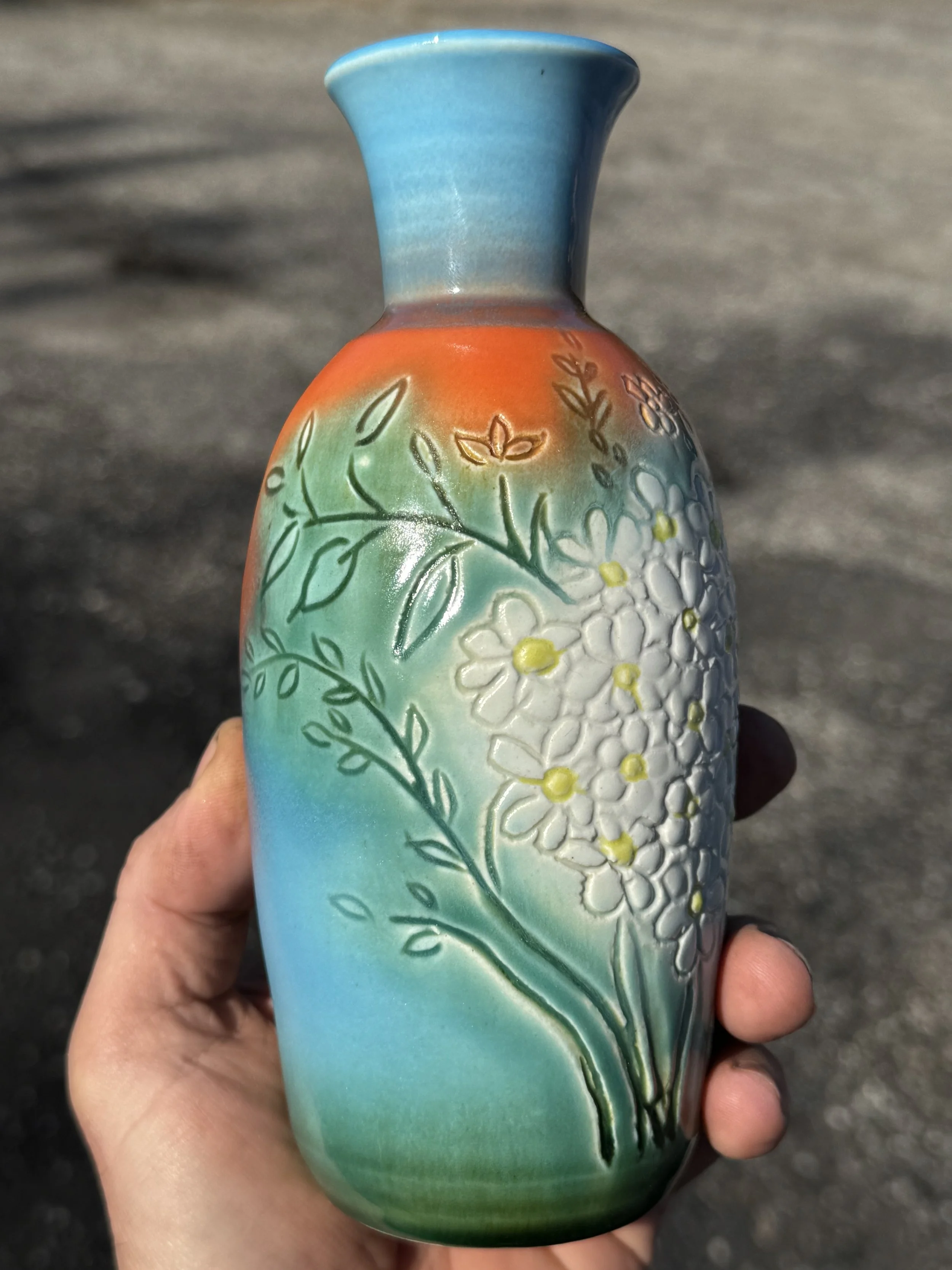 Colorful ceramic vase with floral patterns being held outdoors.