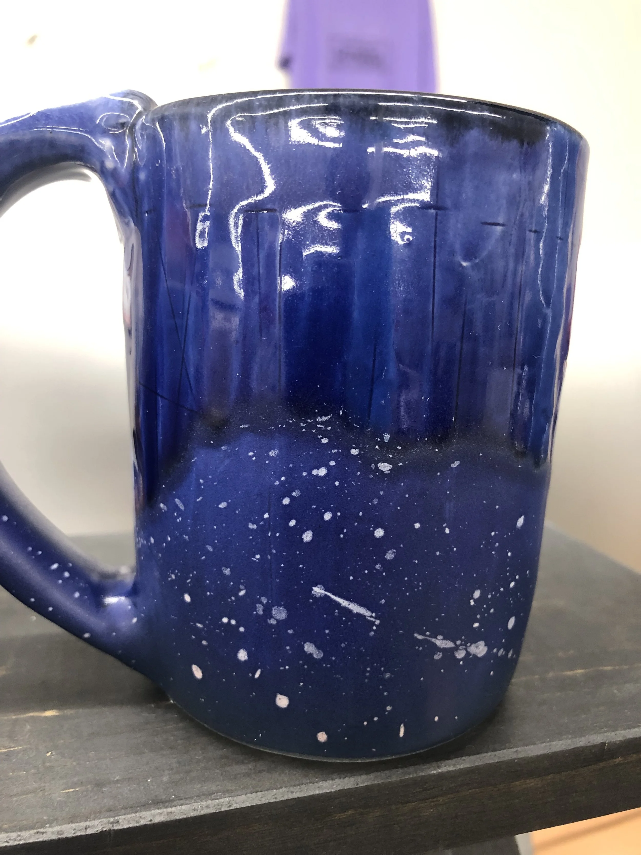 Close-up of a navy blue ceramic mug with a speckled pattern, placed on a dark wooden surface.