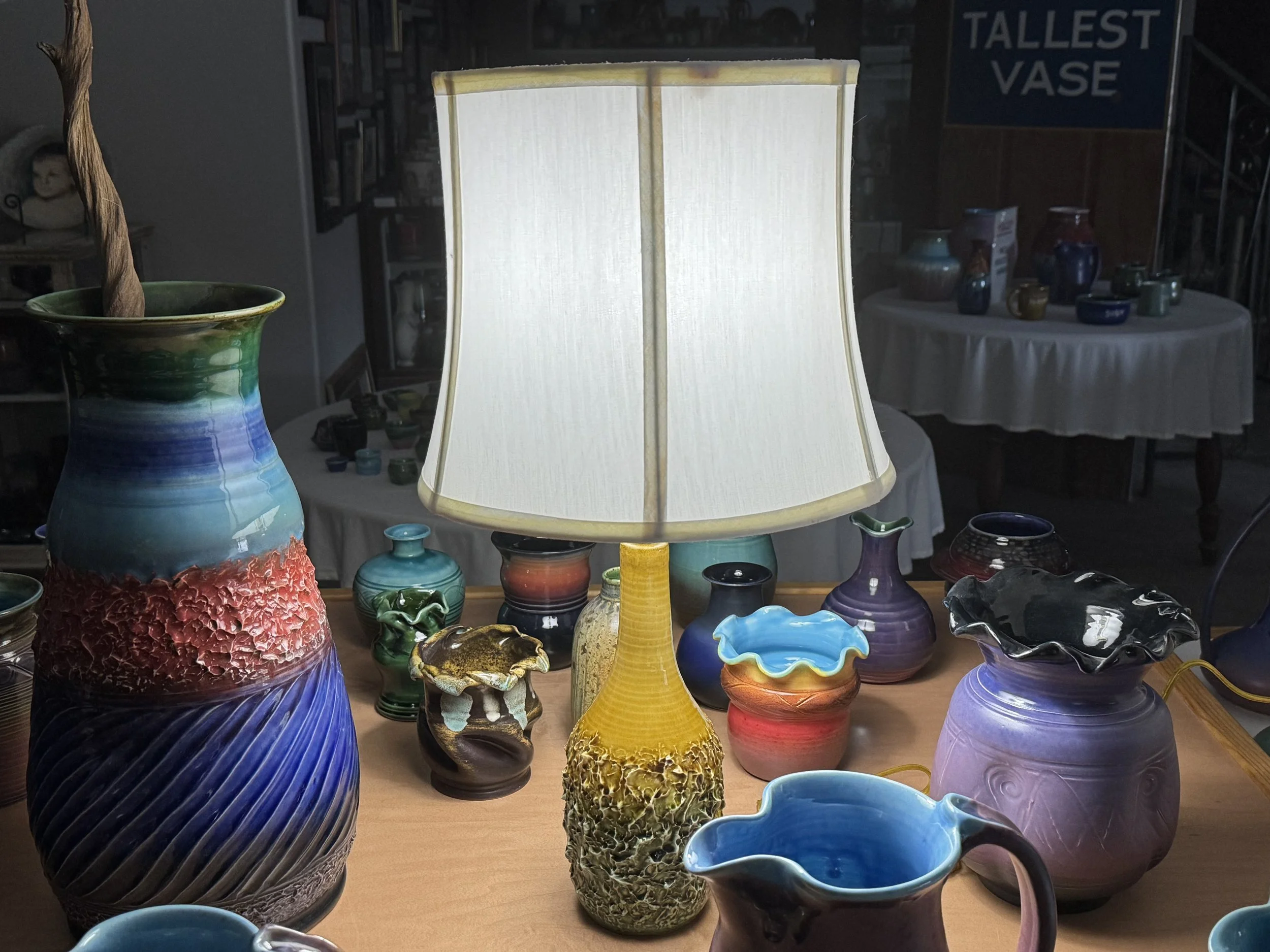 A collection of colorful ceramic vases and pottery displayed on a wooden table with a table lamp in the center.