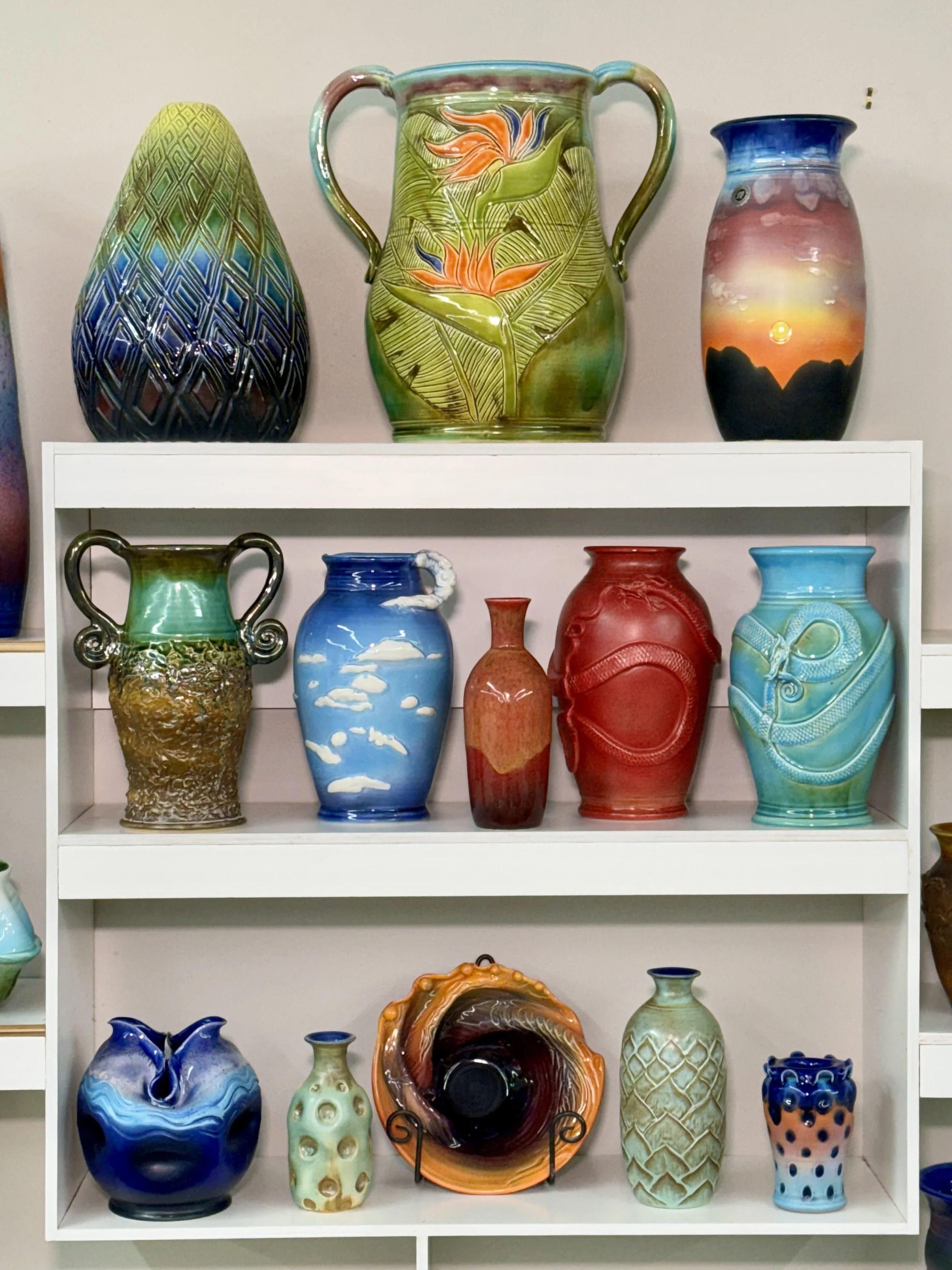 Colorful ceramic vases displayed on white shelves, featuring various shapes, sizes, and decorative designs.