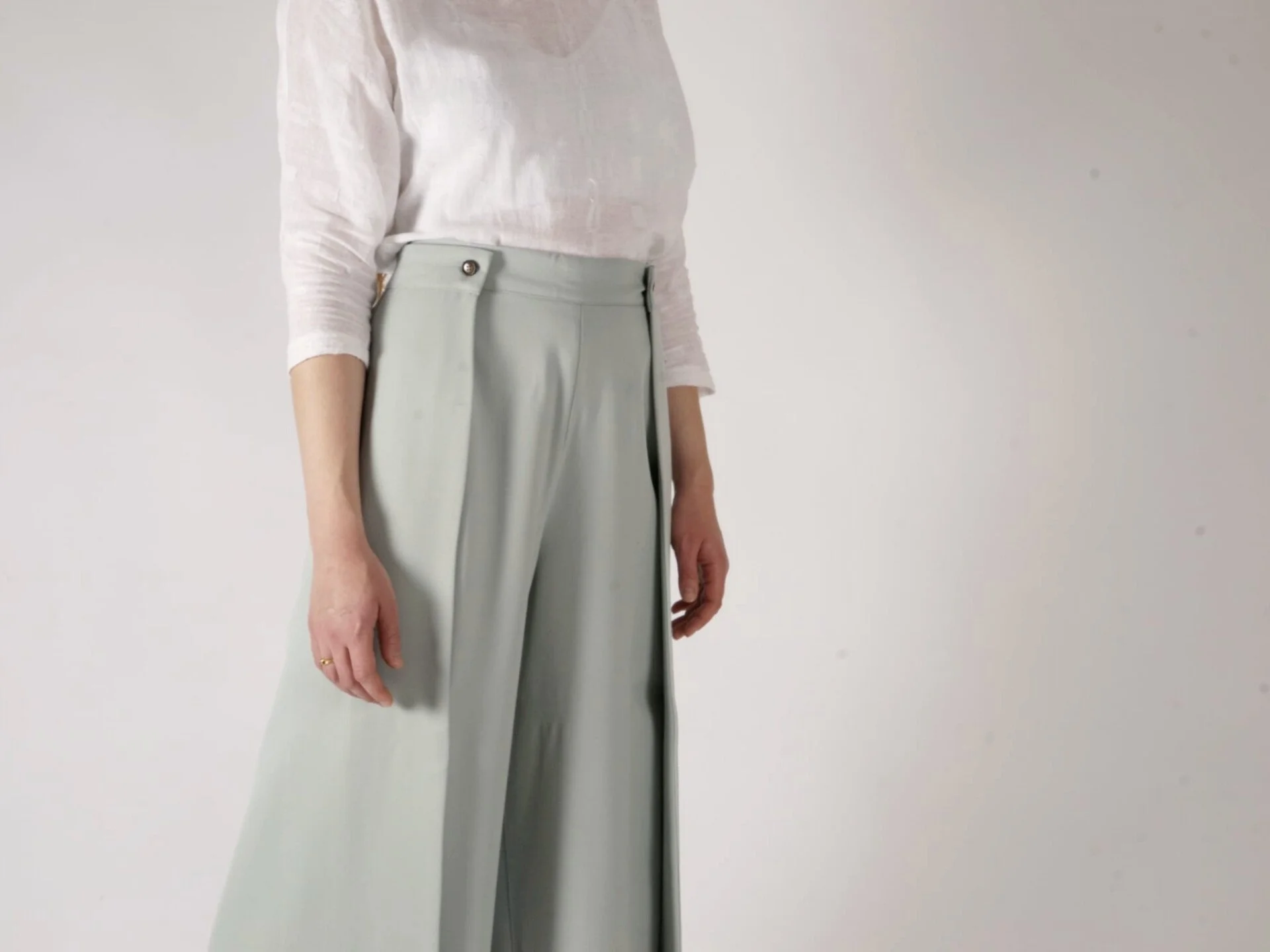 Person wearing a white long-sleeve top and light gray high-waisted wide-leg trousers standing against a plain white background.