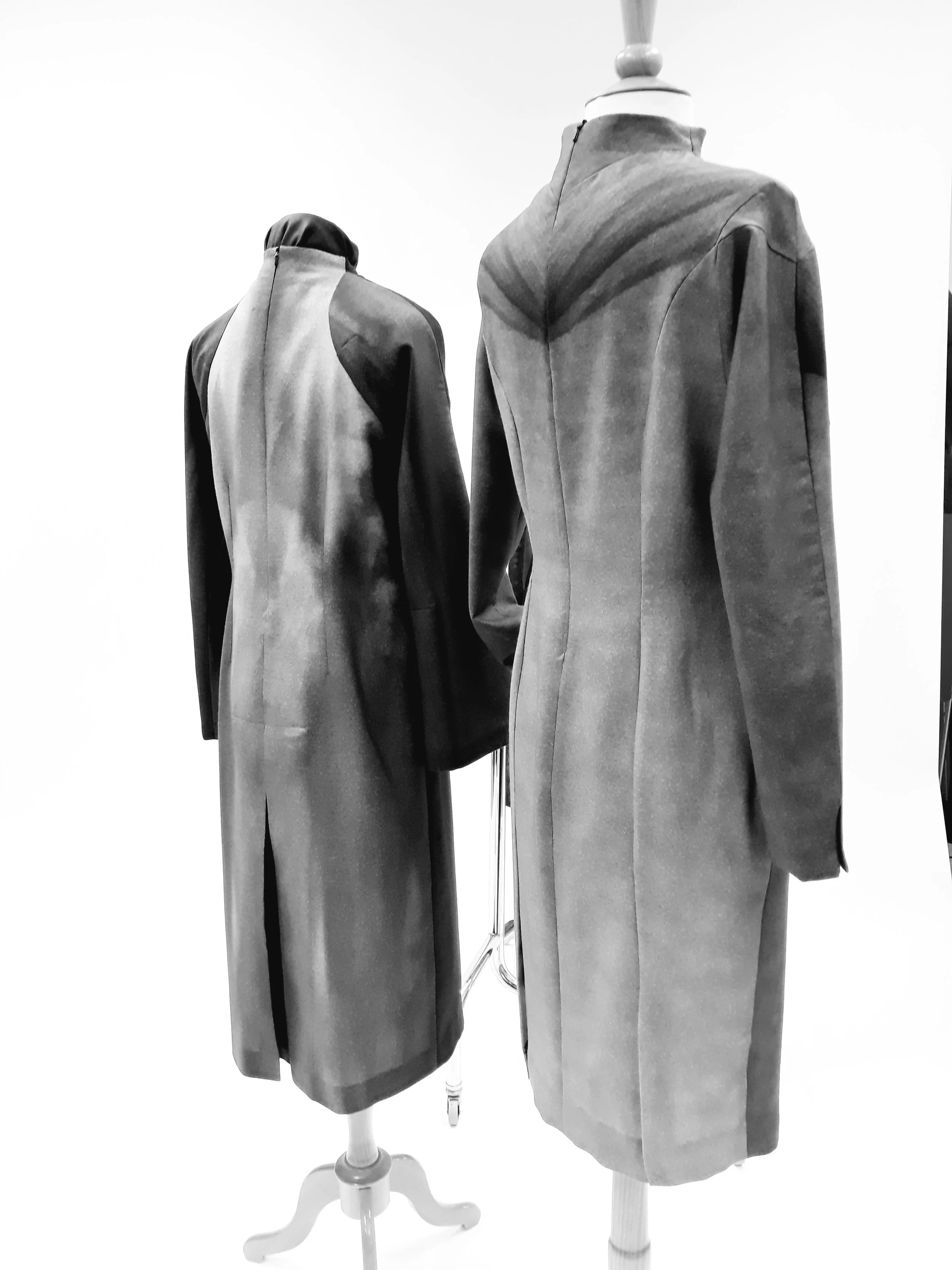 Two mannequins dressed in coats displayed on stands against a white background, with the left mannequin wearing a dark and light gray coat, and the right one in a light gray coat.