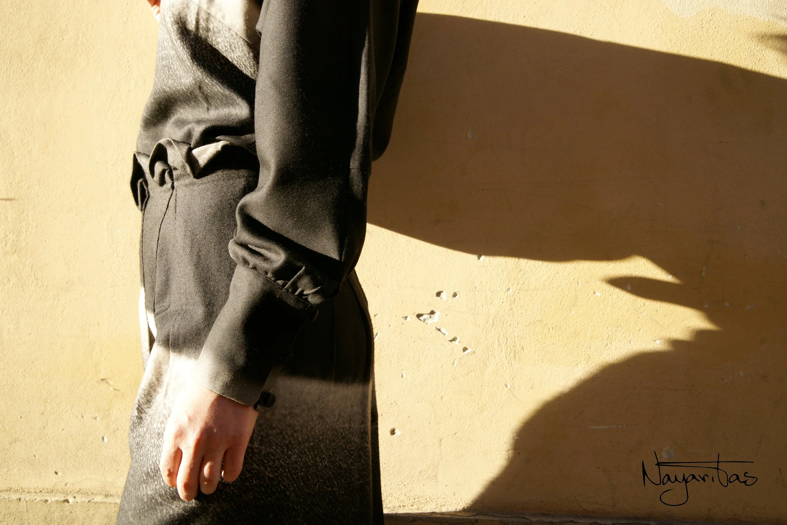 A person wearing black athletic pants standing against a beige wall with sunlight casting a shadow.