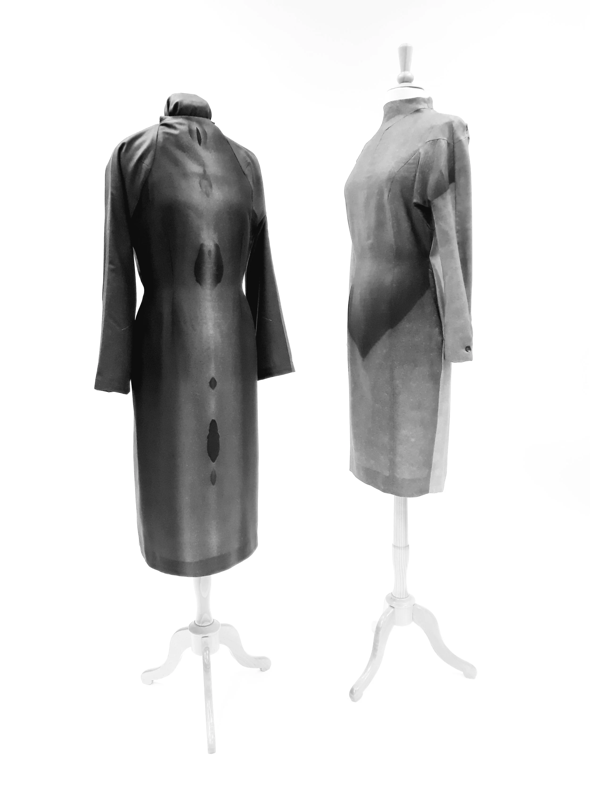 Two vintage dress forms on white stands, one dressed in a long dark coat and the other in a knee-length gray coat, against a plain white background.