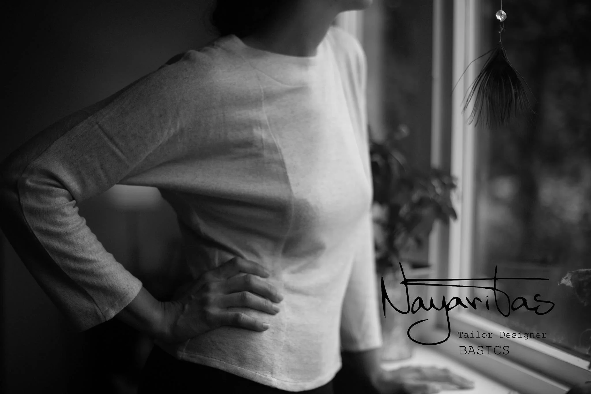 Close-up of a person wearing a light-colored T-shirt with their hand on their hip, standing near a window with a blurred background. The image is in black and white, and there's a handwritten-style text overlay that reads 'Navajas' with smaller text 
