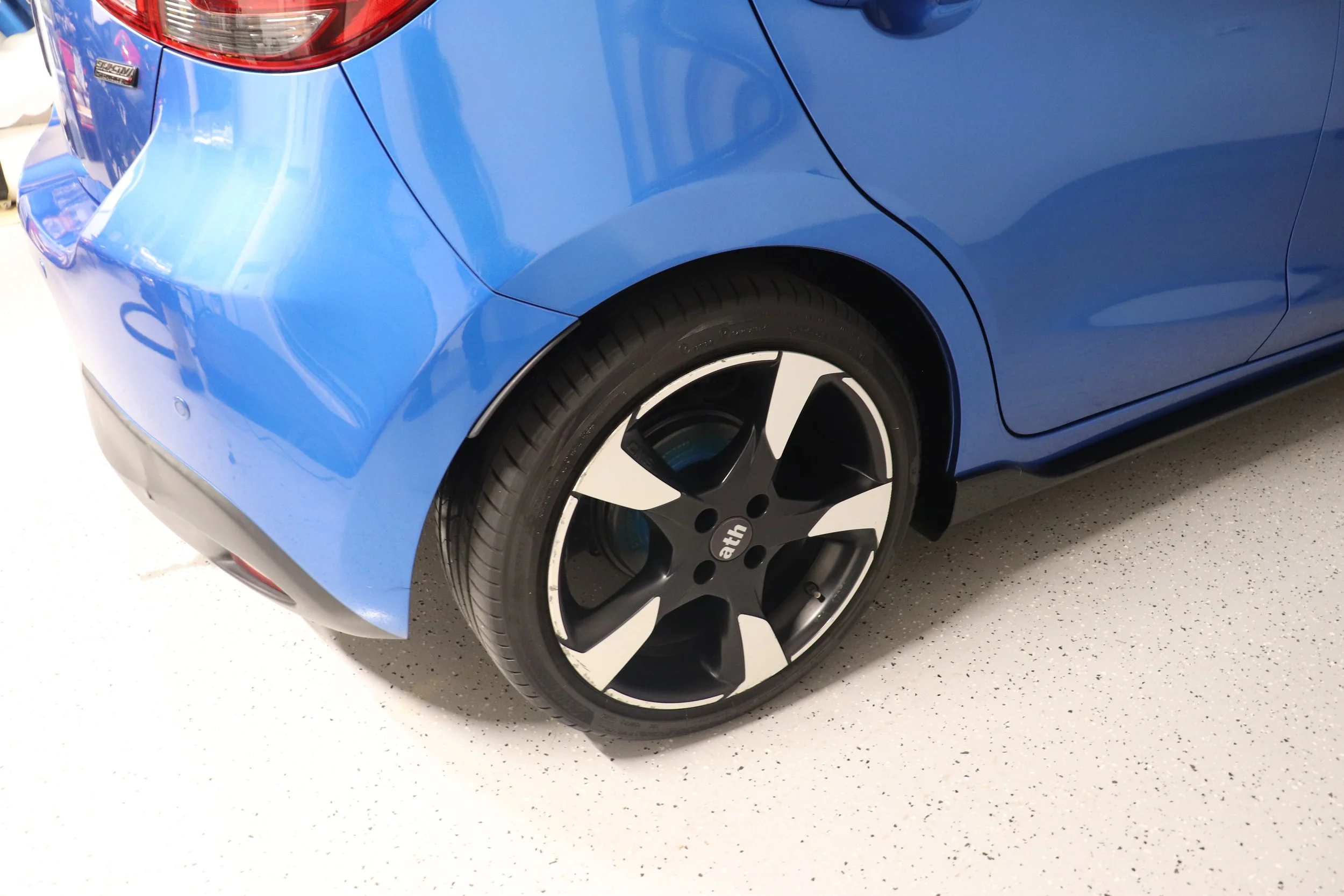 Rear view of a blue car with a stylish black and white alloy wheel.
