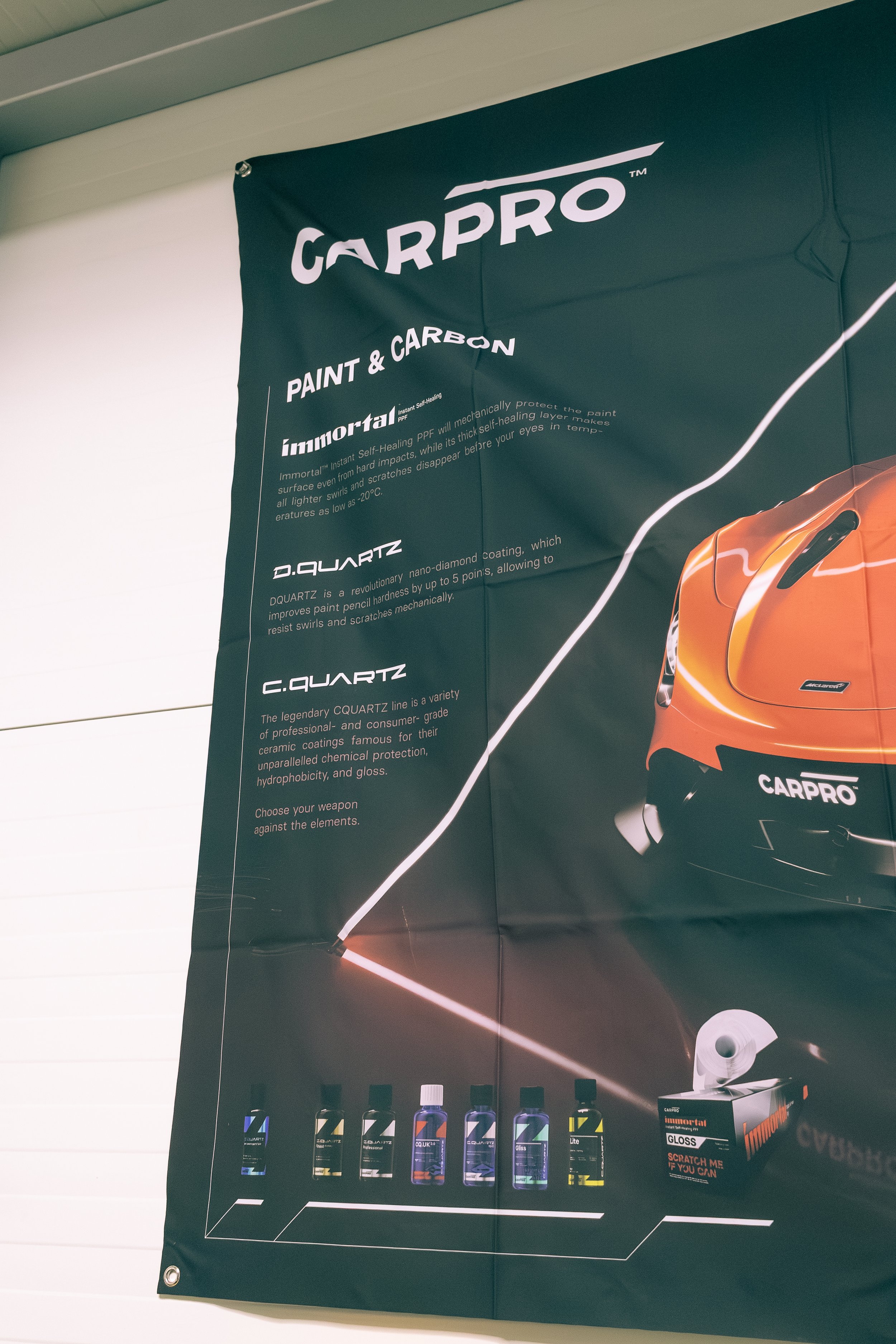 A black banner with white text promoting CarPro paint and carbon products. The top shows the CarPro logo, then details about Immortal Self-Healing Paint Protection Film and D.Quartz nano-diamond coating, with images of various bottles of CarPro produ